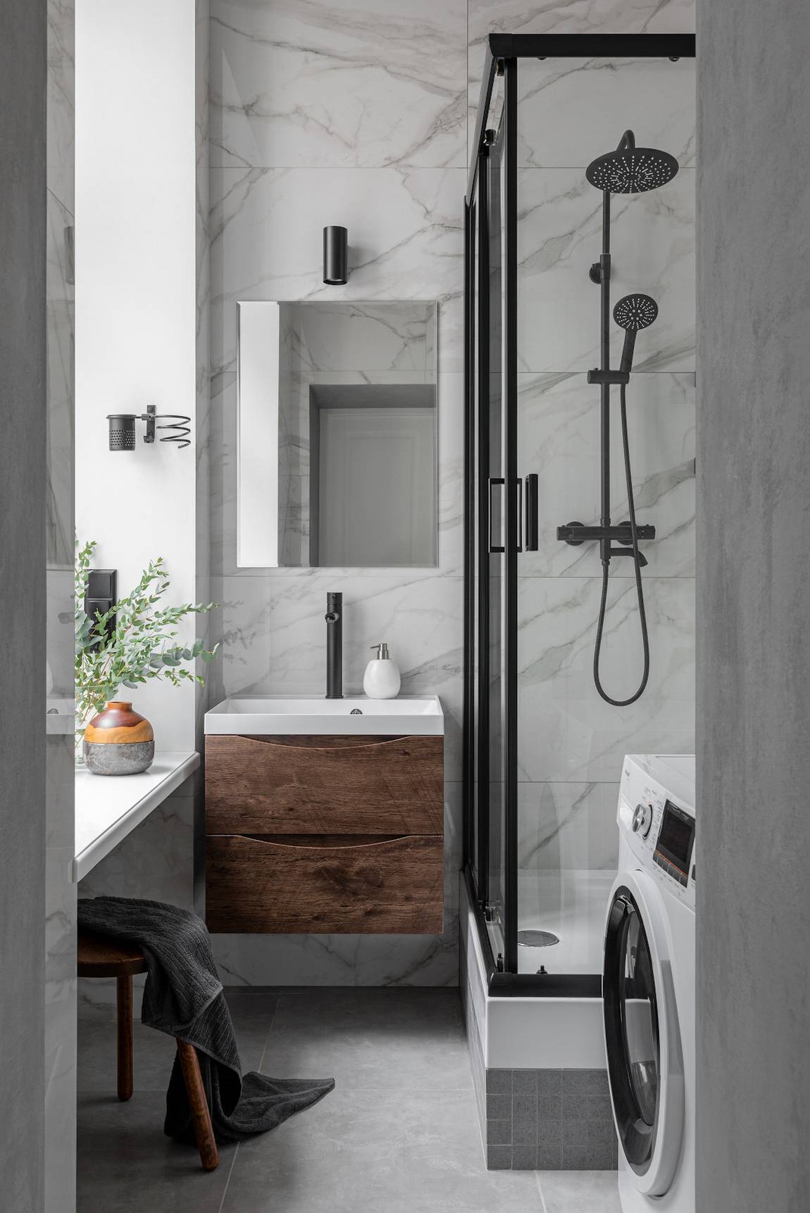 Phòng tắm có diện tích rất nhỏ với chiếc máy giặt được đặt gọn gàng ở góc, buồng tắm nâng cao hơn so với mặt sàn khoảng 50cm, phân vùng với bồn rửa bằng của kính trượt trong suốt.