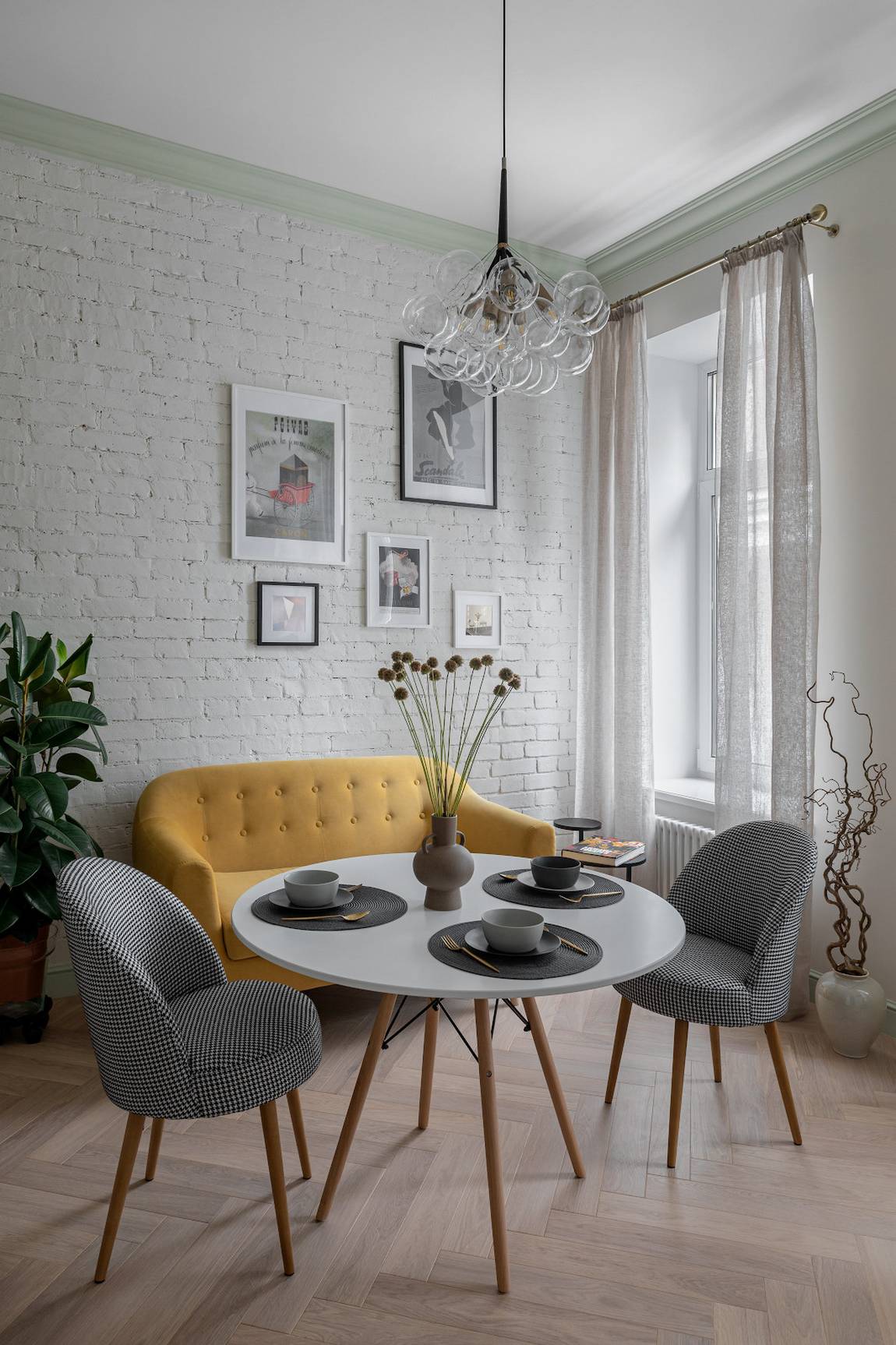 Khu vực phòng khách mang đậm dấu ấn phong cách Scandinavian với sàn gỗ họa tiết xương cá, ghế sofa màu vàng mù tạt nổi bật trước bức tường ốp gạch sơn trắng cùng những khung ảnh nhỏ xinh trang trí.