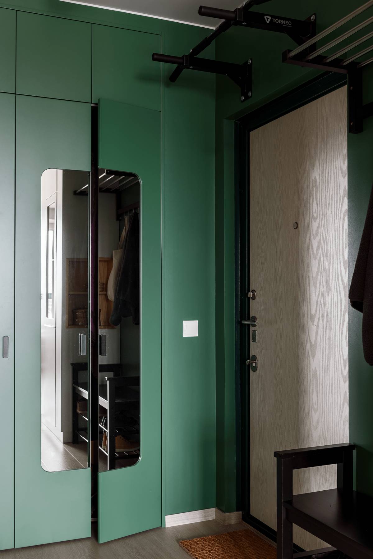 Lối vào căn hộ với cánh cửa gỗ sáng màu, nổi bật giữa chiếc tủ lưu trữ cao kịch trần sơn màu xanh ngọc lục bảo thời thượng. Cánh cửa tủ ốp gương soi cũng góp phần tạo cảm giác nới rộng khu vực này cho thị giác.