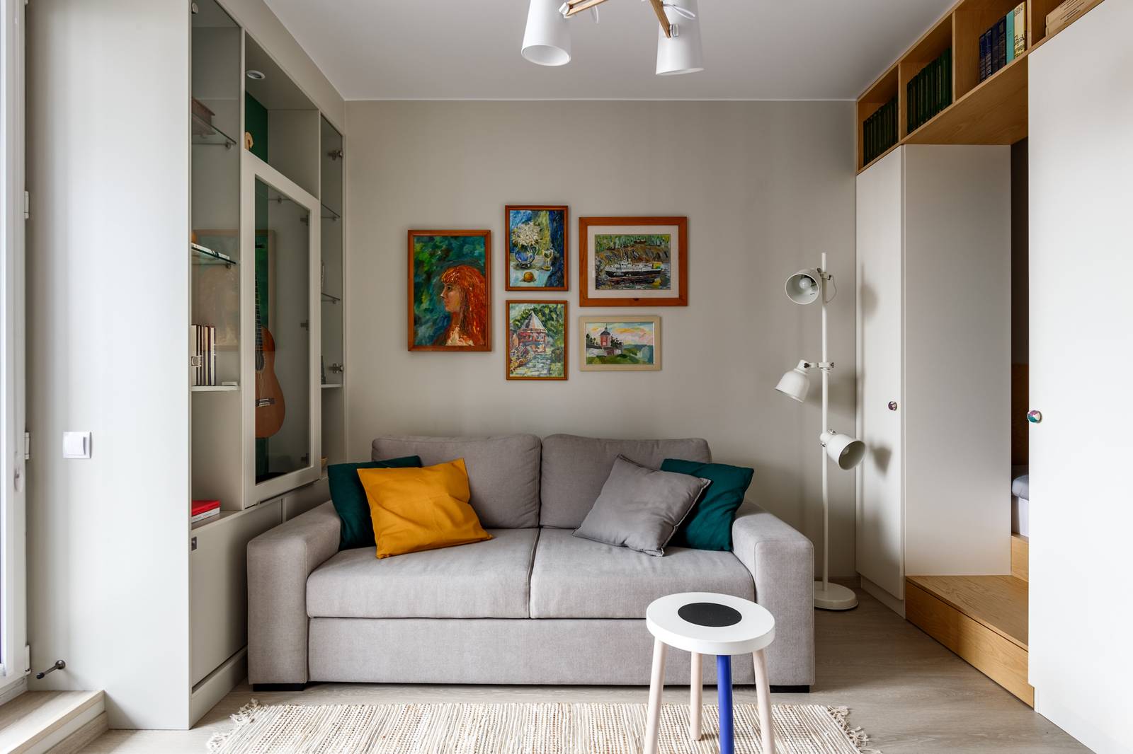 Phòng khách với ghế sofa xám êm ái làm phông nền cho gối tựa màu xanh, vàng mù tạt thêm nổi bật. Trên tường là những bức tranh rực rỡ sắc màu do chính tay chủ nhân vẽ nên.