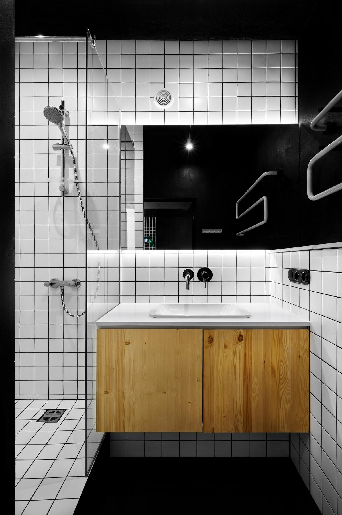 Tường phòng tắm ốp gạch màu trắng ô vuông nhỏ tương tự phòng bếp, phần tường sơn đen lắp đặt những chiếc móc kim loại cố định để treo khăn tắm, quần áo cần thay,...
