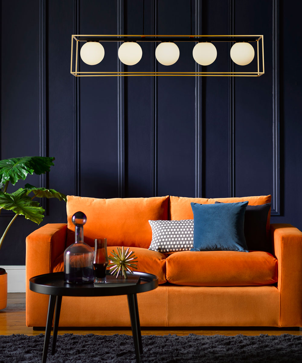 Chiếc ghế sofa với màu cam của những quả quýt chín mọng trở nên nổi bật trên phông nền màu xanh lam đậm ở bức tường phía sau, tạo nên sự tương phản cực kỳ mạnh mẽ, cá tính cho phòng khách.