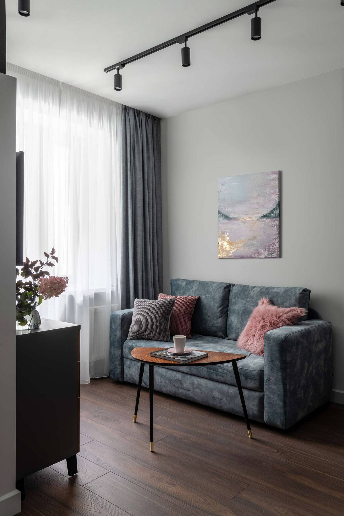 Phòng khách với chiếc ghế sofa đôi êm ái, bên cạnh ô cửa sổ lắp rèm che nhẹ nhàng, bức tranh trừu tượng và đặc biệt là chiếc bàn nước hình bán nguyệt độc đáo.