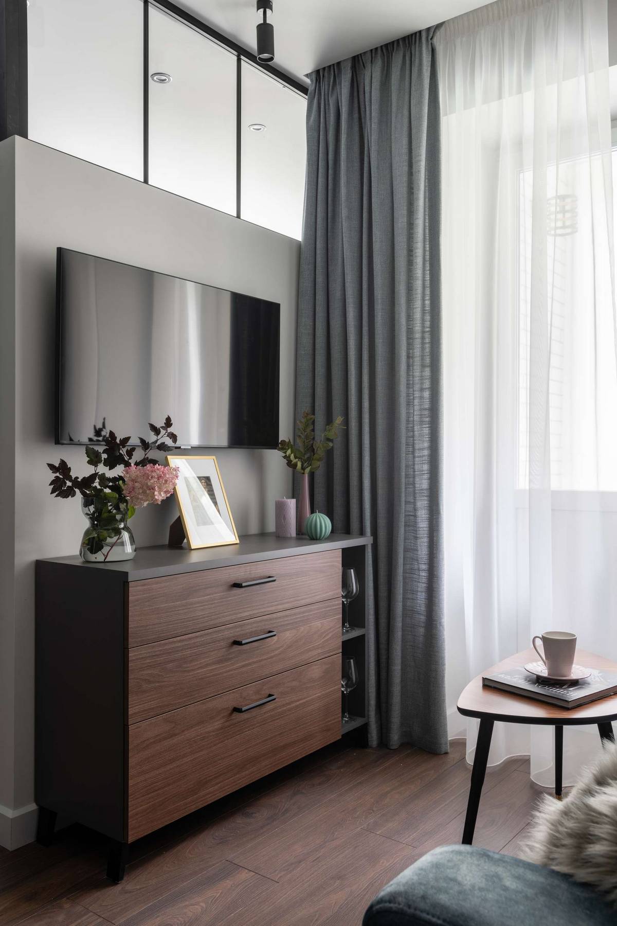Đối diện sofa là chiếc tủ lưu trữ thiết kế theo phong cách truyền thống với 3 ngăn to rộng, tivi gắn tường, trên cao lắp đặt cửa kính thông suốt với phòng ngủ.