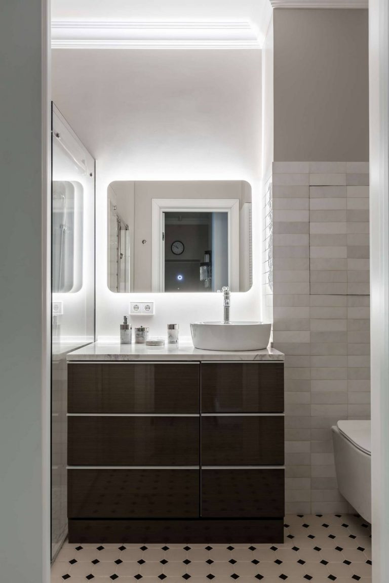 Phòng tắm sử dụng gạch thẻ metro ốp tường màu sáng tạo sự tương phản với tủ lưu trữ màu nâu đen và sàn nhà lát gạch ô vuông nhỏ xinh. Tấm gương hình chữ nhật bo tròn các cạnh giúp căn phòng rộng hơn so với diện tích thật.