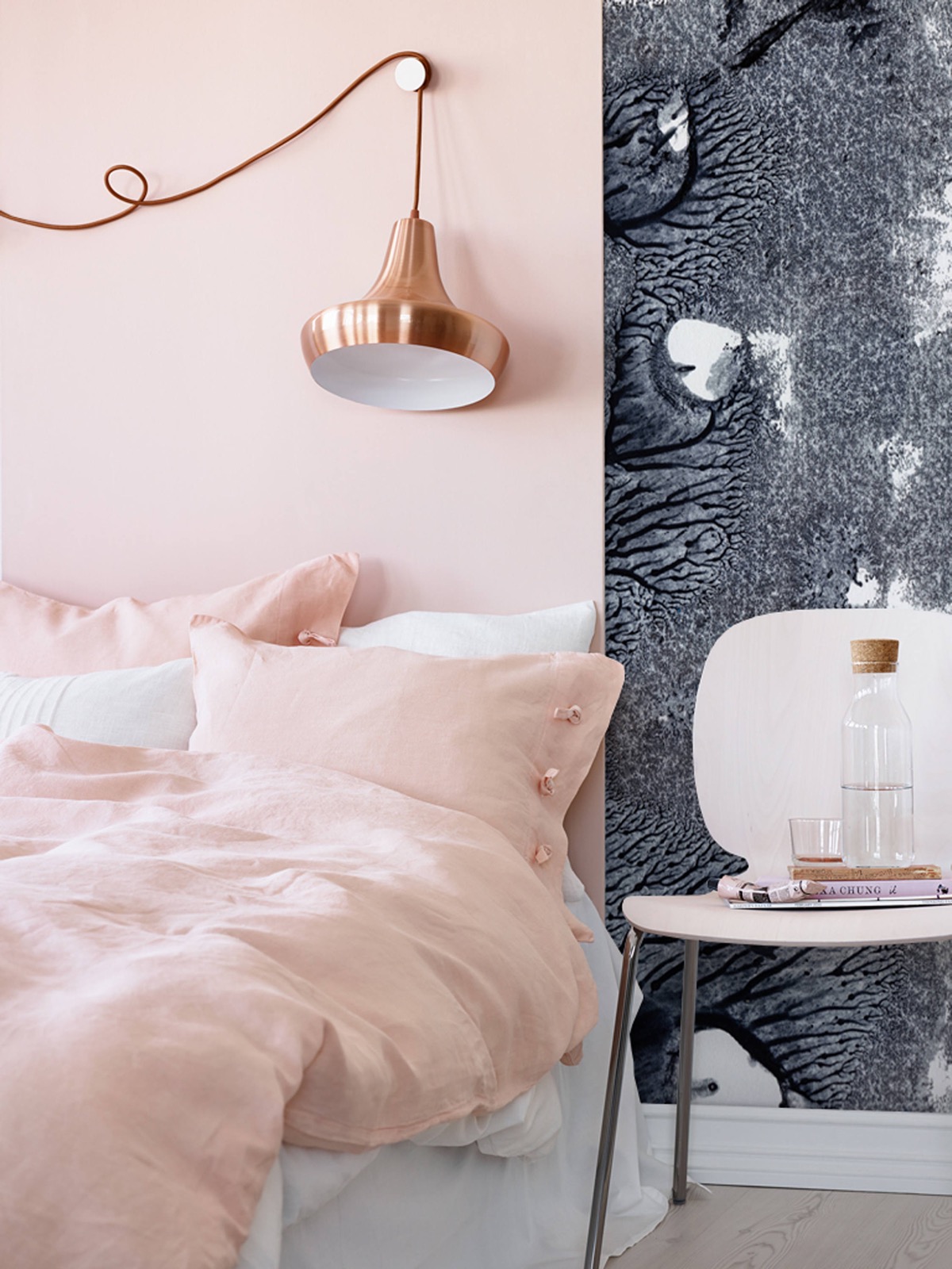 Bộ chăn gối màu hồng pastel mềm mại nổi bật trên ga trải giường màu trắng tinh khôi tạo nên vẻ đẹp nữ tính. Bức tường chia thành hai phần với gam màu hồng và xám cho sự tương phản nhẹ nhàng. Đặc biệt nhất là chiếc đèn thả trần sắc sảo, bóng đẹp.