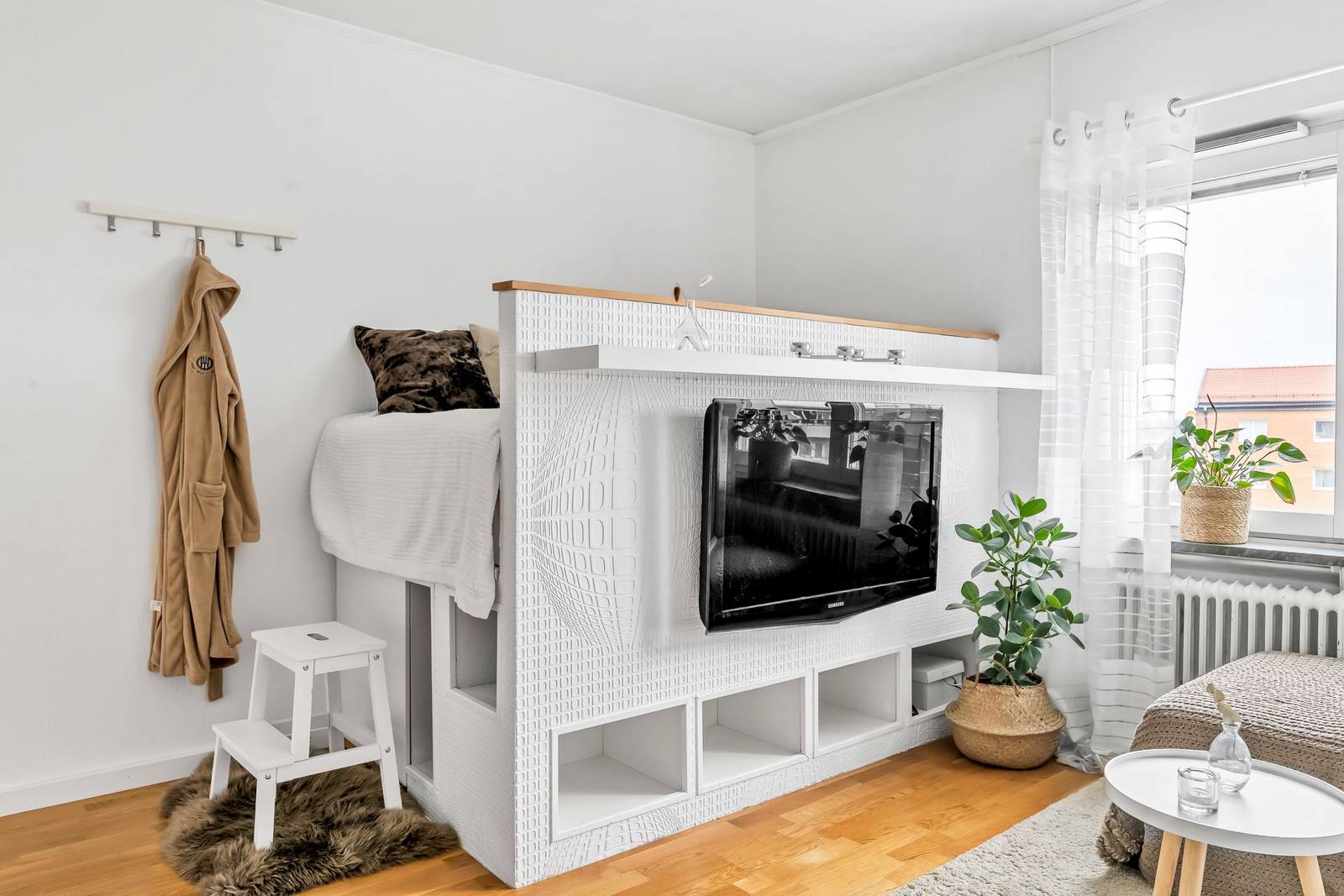 Chính chiếc giường ngủ độc đáo nào đã tối ưu hóa không gian căn hộ với diện tích sàn nhỏ, trần nhà thấp nhưng vẫn tạo sự riêng tư nhất định cho không gian nghỉ ngơi. Bên dưới là khu vực lưu trữ thoải mái, thêm cả móc treo quần áo nhỏ gọn và kệ mở trên tivi.