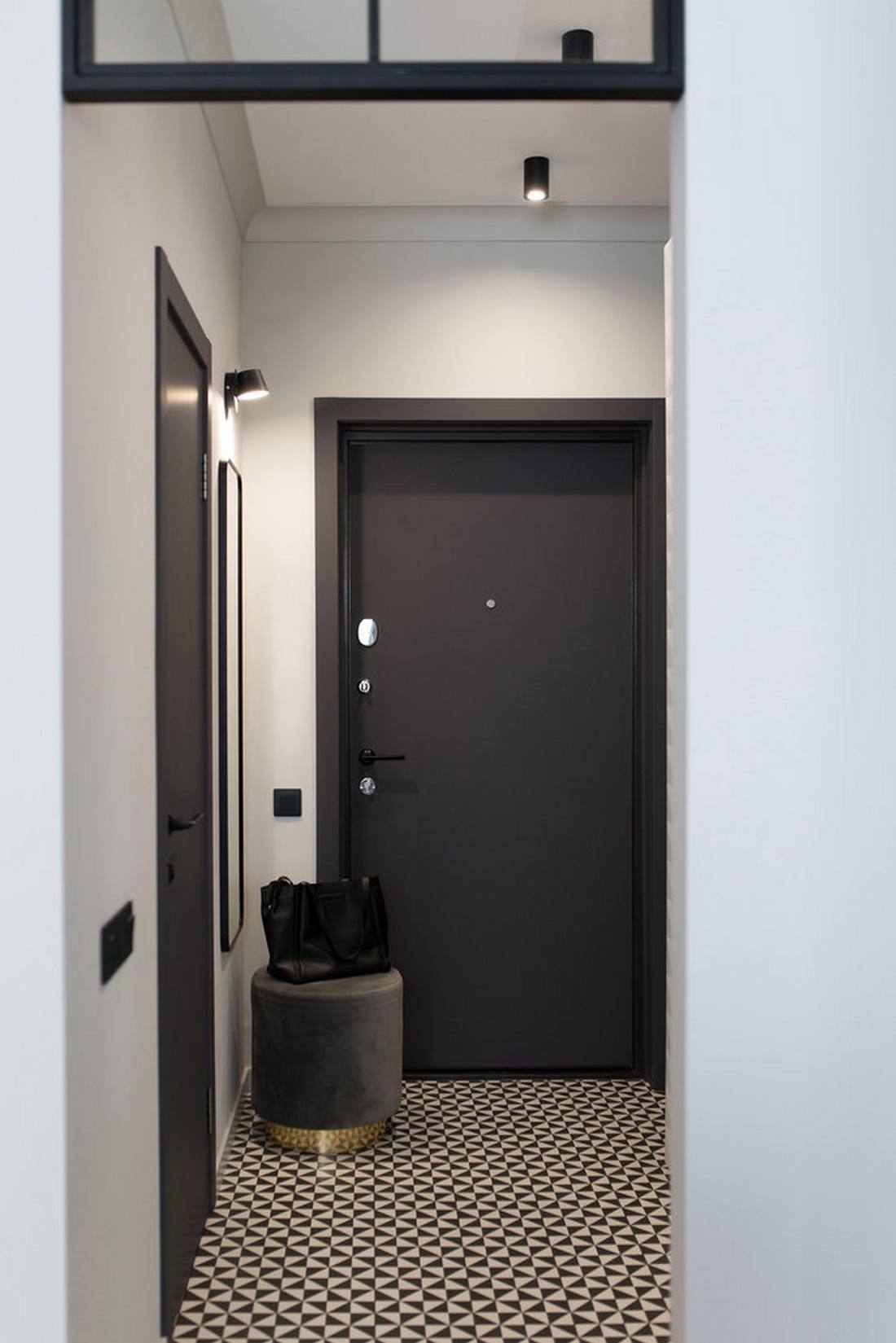 Lối vào căn hộ sử dụng hai gam màu trắng - đen cổ điển tạo cảm giác tò mò ngay từ cái nhìn đầu tiên. Tấm gương soi lắp dọc bức tường, sau chiếc ghế đôn nghỉ chân cùng với gạch bông lát sàn họa tiết truyền thống.