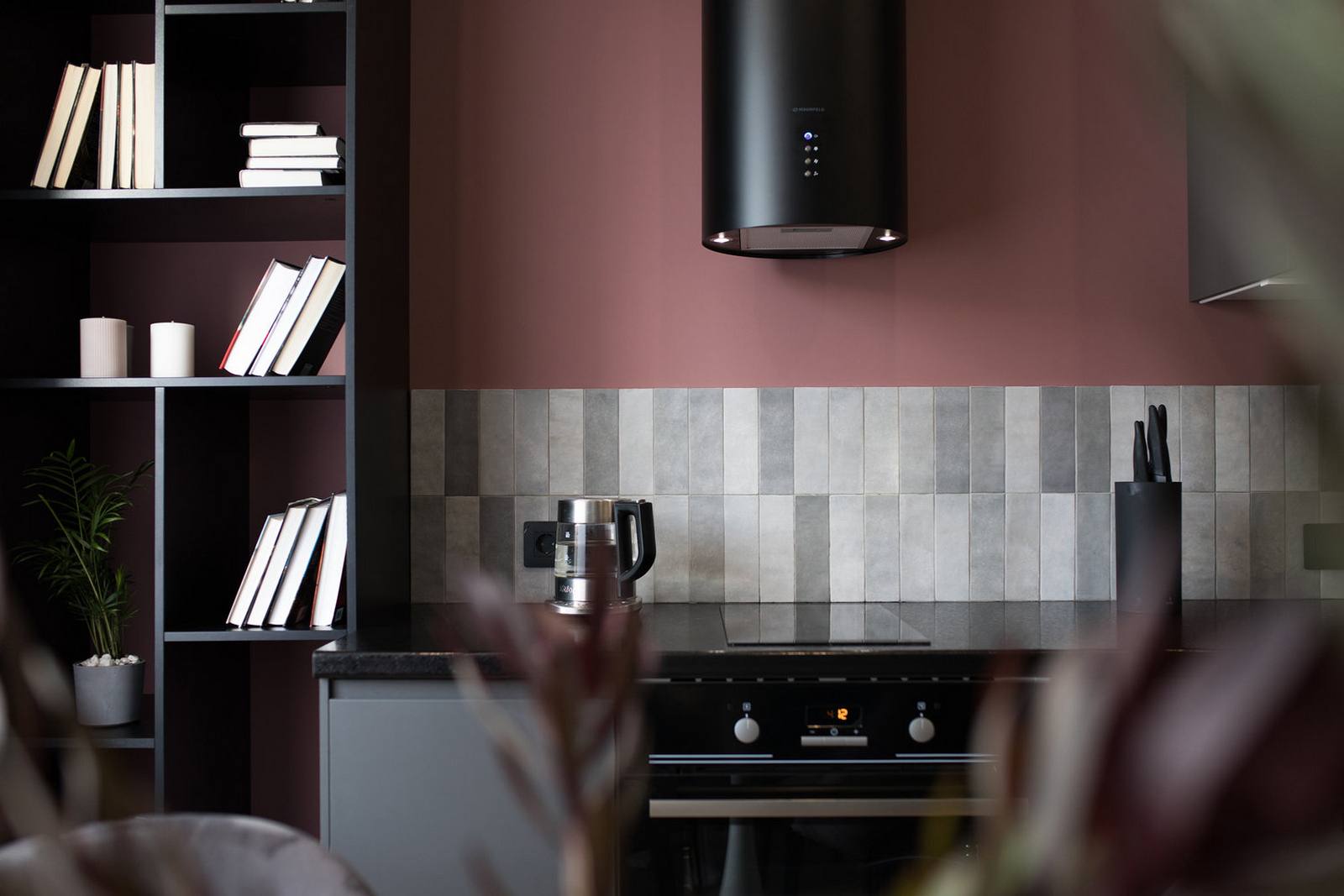 Tường phòng bếp sử dụng sơn màu hồng đất cho cảm giác ấm áp, nổi bật những viên gạch hình chữ nhật xếp dọc khu vực backsplash, bên trên là thiết bị hút mùi hiện đại cùng tông màu đen sắc sảo.