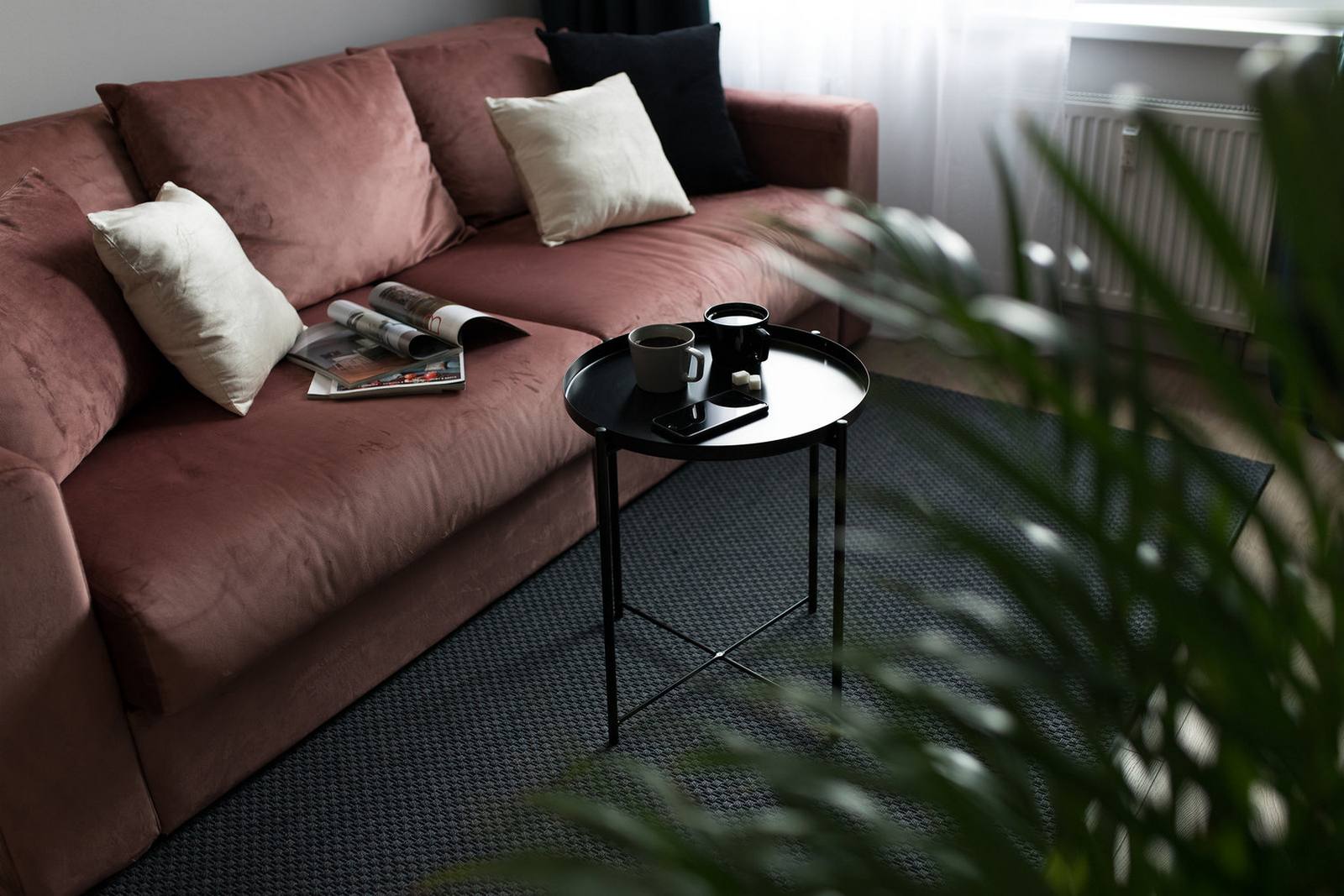 Phòng khách với chiếc ghế sofa màu hồng đất cho cảm giác ấm cúng, thân mật, nổi bật trên tấm thảm trải sàn màu xám đậm và nền tường xám nhạt đằng sau. Một chậu cây cảnh đặt ngay cửa trượt cũng giúp không gian tươi trẻ hơn.
