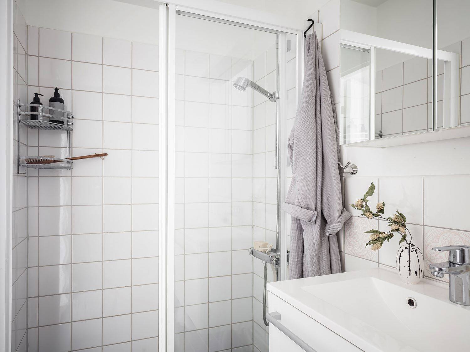 Khu vực buồng tắm đứng được phân vùng bởi cửa trượt bằng kính trong suốt. Kệ góc bằng inox trên tường giúp lưu trữ gọn gàng, tận dụng hiệu quả góc tường trong phòng nhỏ.
