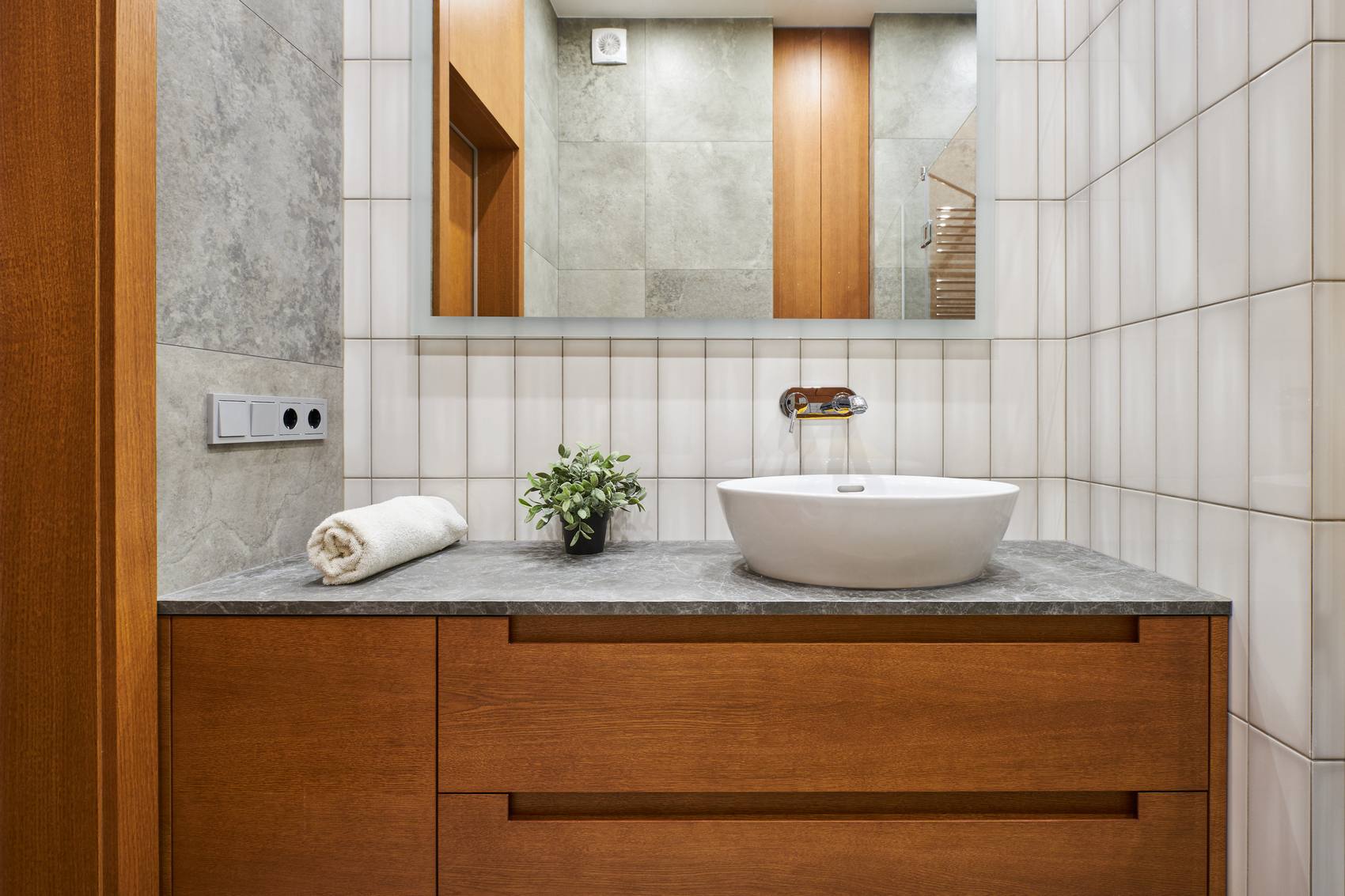 Gạch ốp tường phòng tắm được chia thành 2 mảng, một bên sử dụng gạch xi măng màu xám tương đồng với sàn nhà, phần còn lại ốp gạch thẻ dọc màu trắng với về mặt sáng bóng.