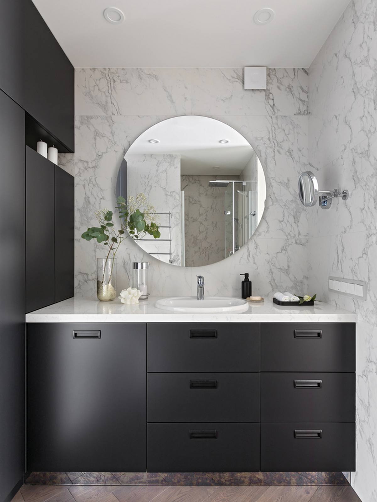 Tương tự phòng bếp, phòng tắm cũng sử dụng hệ tủ lưu trữ màu xám để tạo cái nhìn mạnh mẽ, đồng thời trung hòa sắc xanh lá cây và tím trong căn hộ. Tấm gương hình tròn trên nền tường đá cẩm thạch giúp không gian như 'nhân đôi' bằng thị giác.