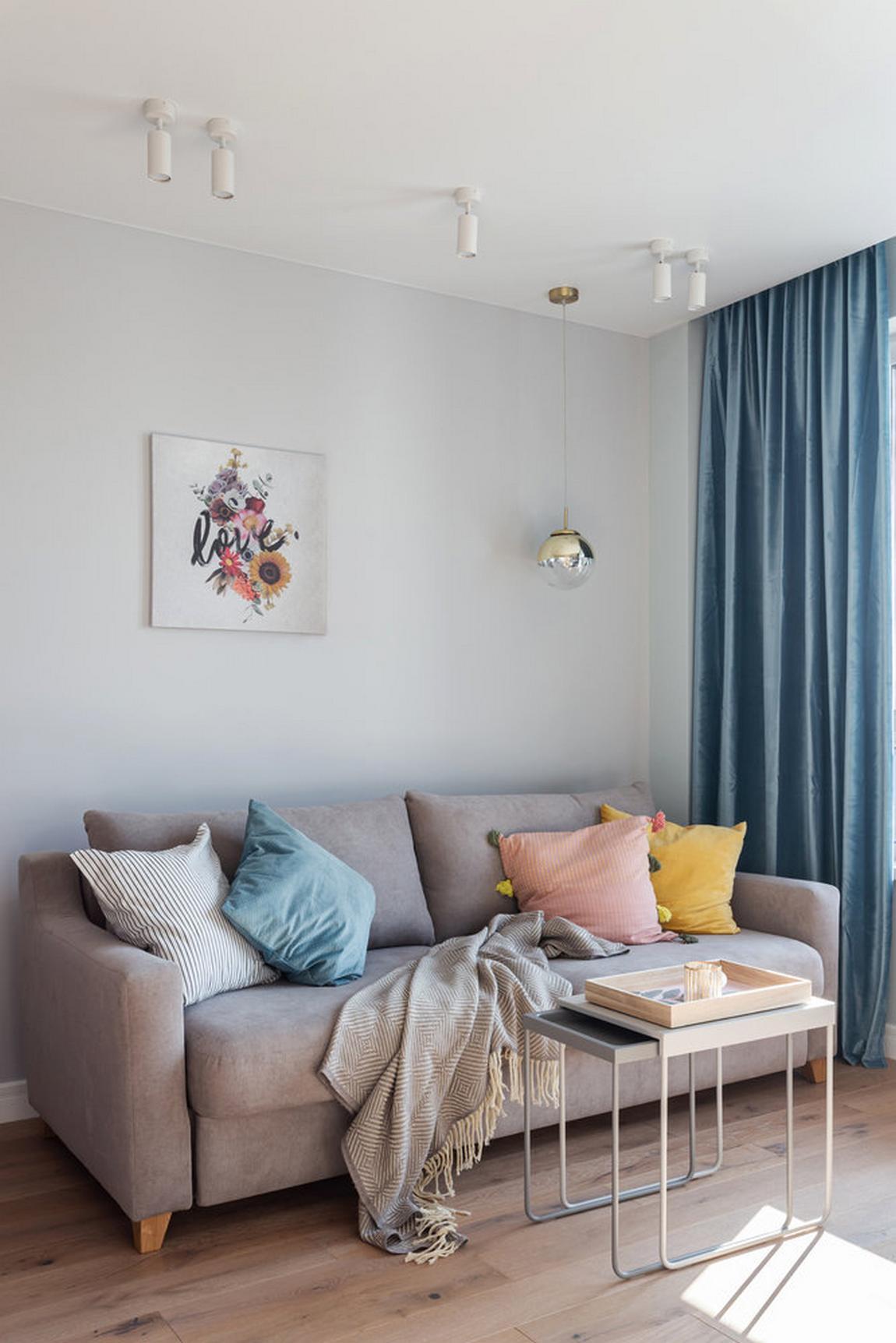 Phòng khách có thiết kế nội thất đơn giản nhưng sinh động về màu sắc. Chiếc ghế sofa màu xám với bộ sưu tập gối tựa 4 màu hồng, vàng, xanh, trắng dễ thương. Chiếc bàn nước '2 trong 1' cũng tăng thêm tính tiện ích và gọn gàng cho căn hộ.