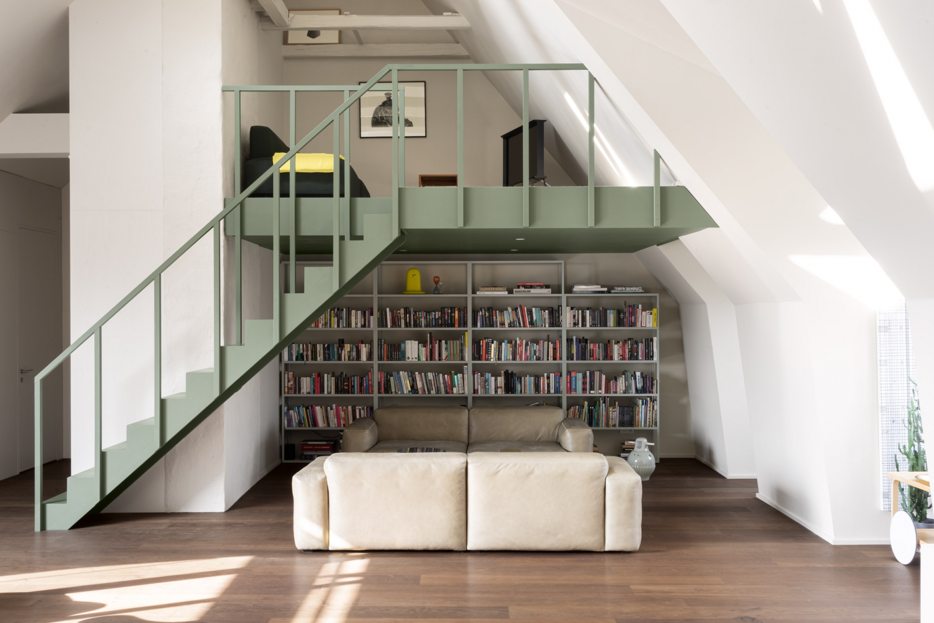 Phòng khách trang trọng với 2 chiếc ghế sofa cỡ lớn bọc da màu trắng kem đặt đối diện nhau. Phía sau là một giá sách cao làm thành một “thư viện mini” trong nhà nhỏ.