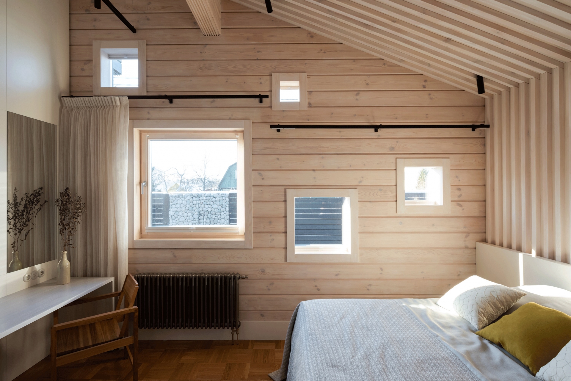 Lam gỗ kéo dài từ trần nhà xuống đầu giường với bức tường gỗ tươi sáng, tương phản nhẹ nhàng với sàn gỗ tối màu thêm phần mộc mạc.