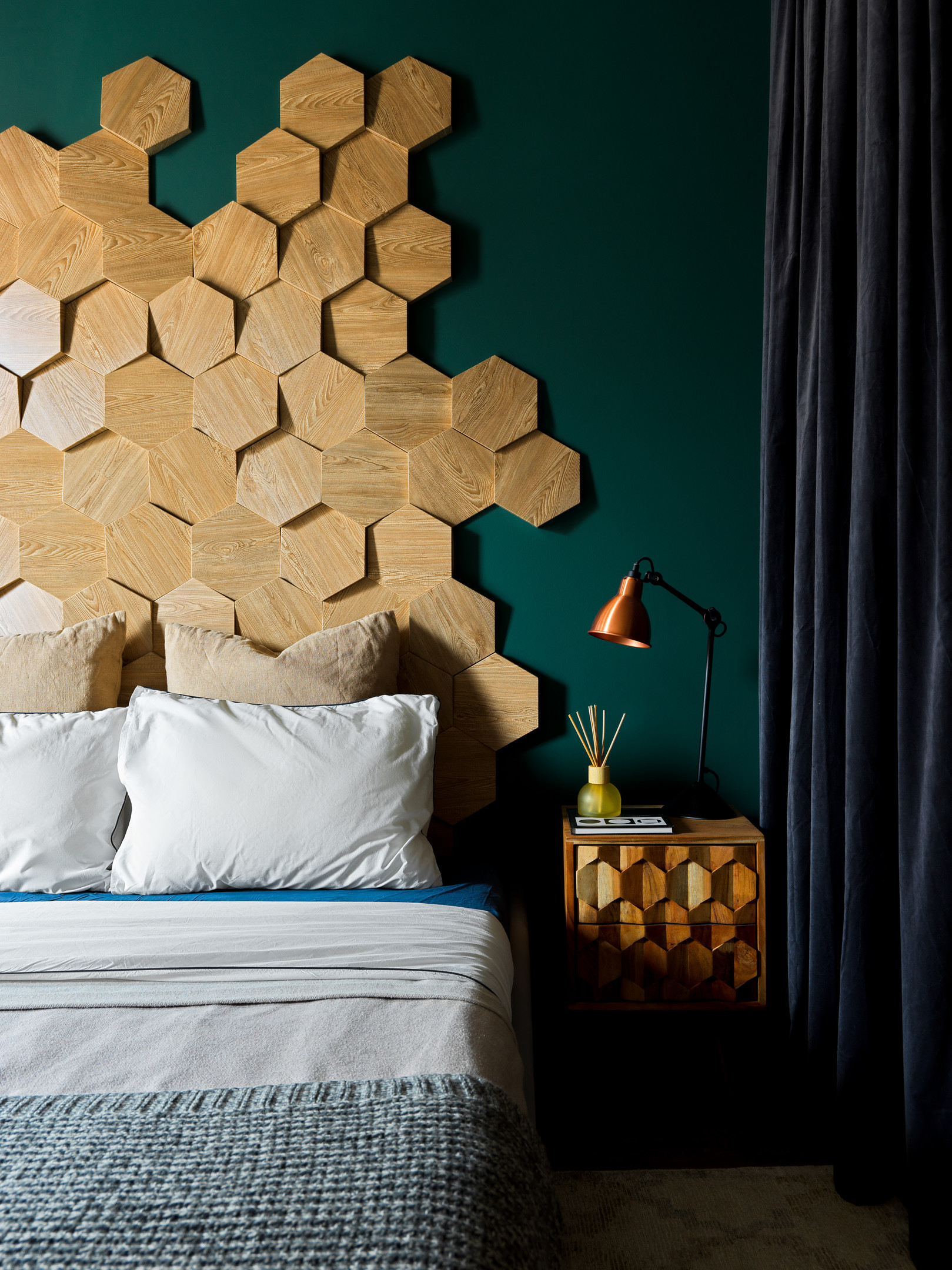 Đầu giường được trang trí bằng những tấm gỗ sáng màu hình lục giác, ghép lại ngẫu hứng thành họa tiết tổ ong bắt mắt. Táp đầu giường lựa chọn thiết kế gắn tường, thêm cả đèn đọc sách tiện lợi.