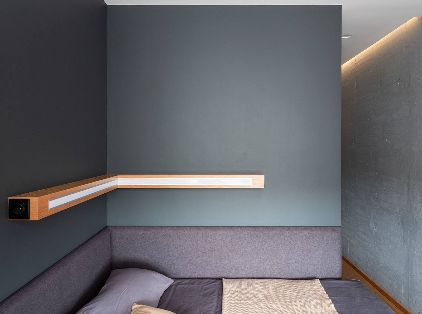 Phòng ngủ có thiết kế siêu đơn giản, có thể nói là tinh giản nội thất đến mức tối đa. Không táp đầu giường, không sử dụng bất cứ phụ kiện trang trí nào, chỉ có duy nhất một thiết bị chiếu sáng tích hợp kệ góc trên nền tường xám.