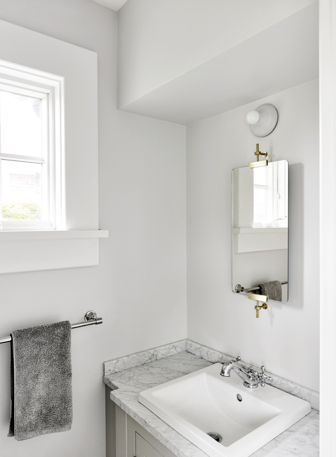 Phòng tắm cũng được sơn màu trắng tươi sáng, tuy nhiên có thêm sự góp mặt của màu xám nhạt trên mặt bàn bằng đá cẩm thạch ở khu vực bồn rửa tay. 