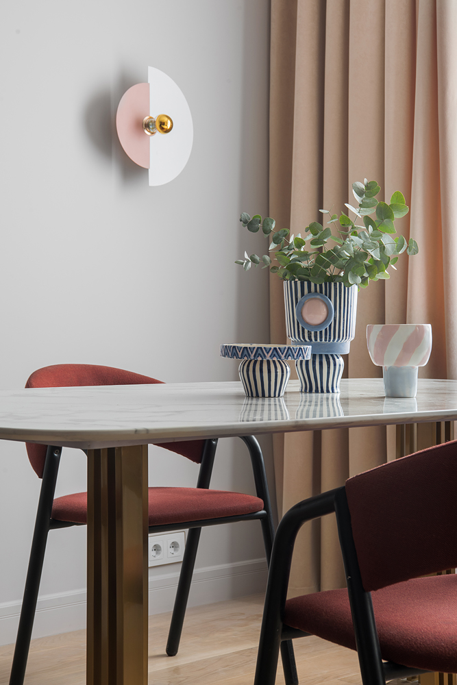 Những chiếc bình hoa bằng gốm sứ họa tiết kẻ sọc đơn giản nhưng hút mắt là tác phẩm của nghệ nhân Anna Miro. Chiếc đèn treo tường kết hợp 2 hình bán nguyệt hồng - trắng trên nền xám đến từ thương hiệu Aromas.