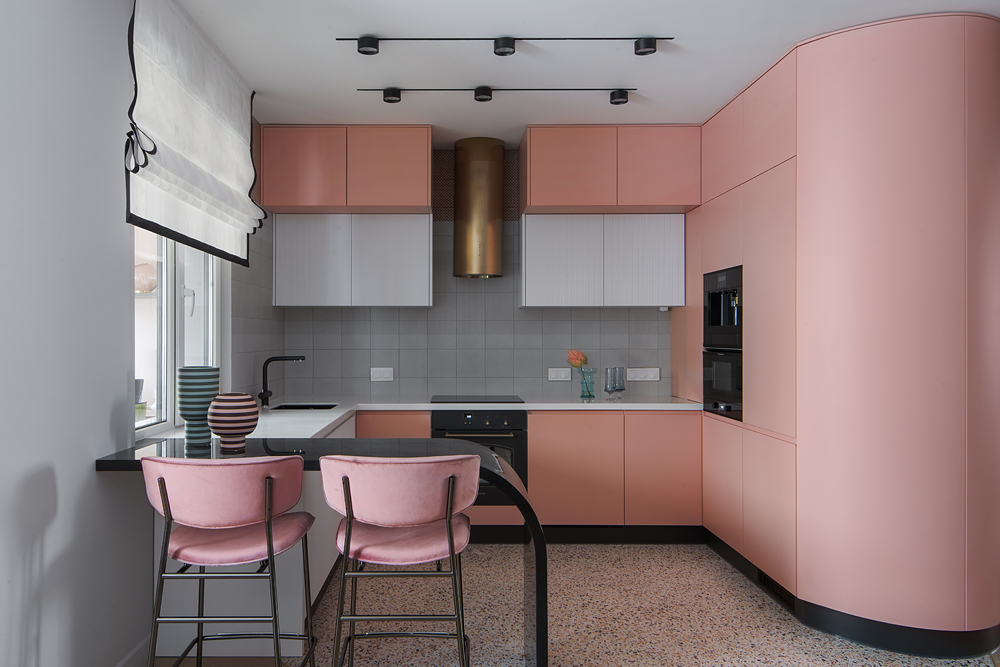 Đối diện bàn ăn là phòng bếp với quầy bar màu đen đường cong đẹp mắt, 2 chiếc ghế màu tone hồng có phần nhạt hơn so với sắc hồng của 4 chiếc ghế ở khu vực ăn uống. Phòng bếp chọn gạch lát sàn họa tiết Terrazzo để dễ vệ sinh và tạo sự phân vùng tự nhiên.