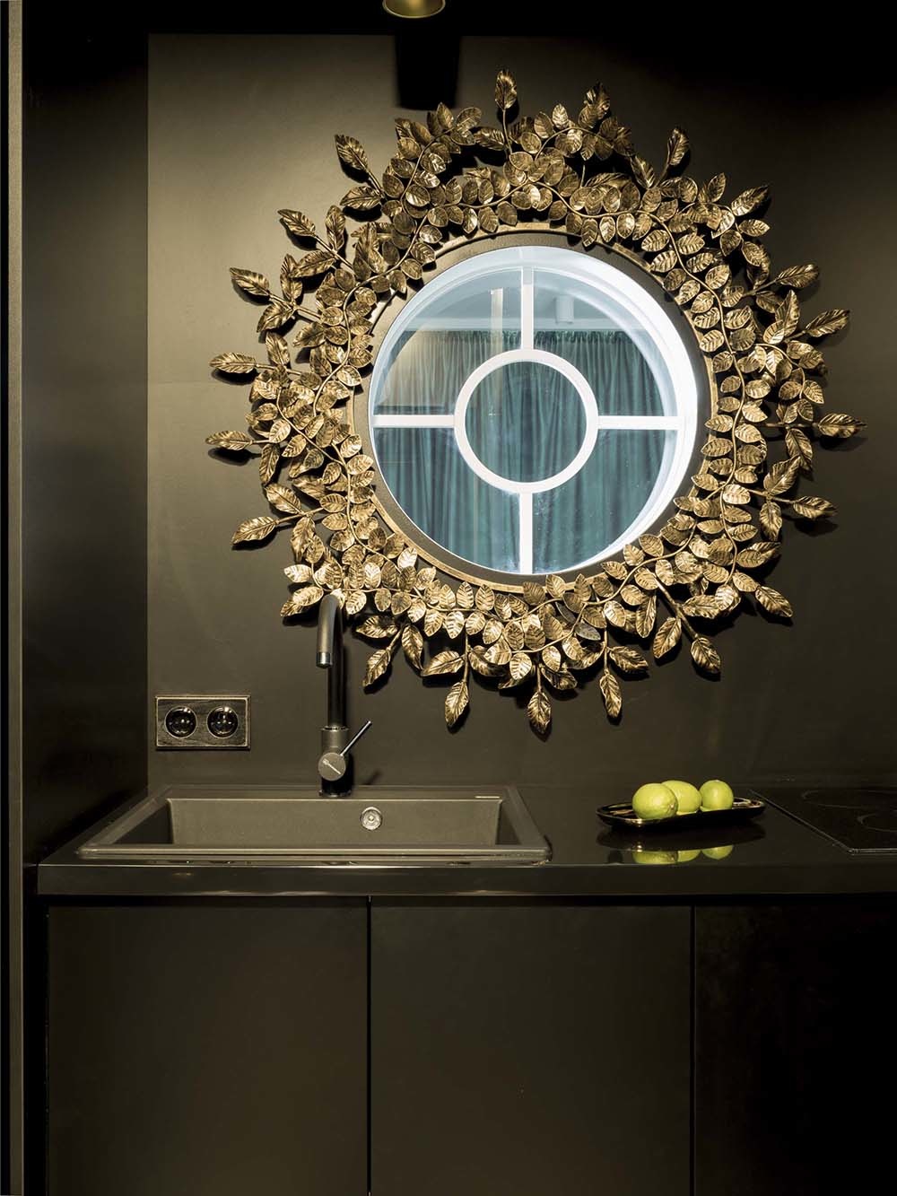 Thoạt nhìn, bạn sẽ ngỡ trên bồn rửa là gương soi như thường thấy đúng không nào? Thật ra, đây là 1 cửa sổ hình tròn kết nối phòng bếp và phòng khách phía bên kia. viền khung là những lá mạ vàng đồng cầu kỳ, bên trong tích hợp đèn chiếu sáng tiện nghi.
