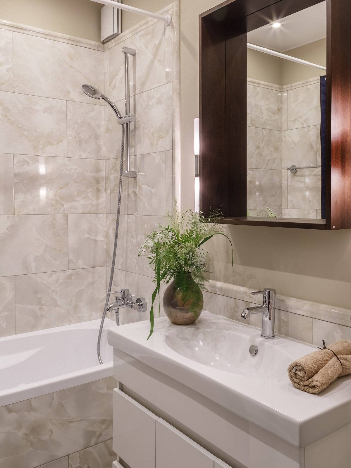 Tường và bồn phòng tắm được ốp đá màu be đường vân nhẹ nhàng, sang trọng. Tủ lưu trữ kết hợp bồn rửa tay bằng sứ sáng bóng. Phía trên là tấm gương giúp phản chiếu không gian và ánh sáng cho căn phòng cảm giác rộng hơn so với diện tích thật.