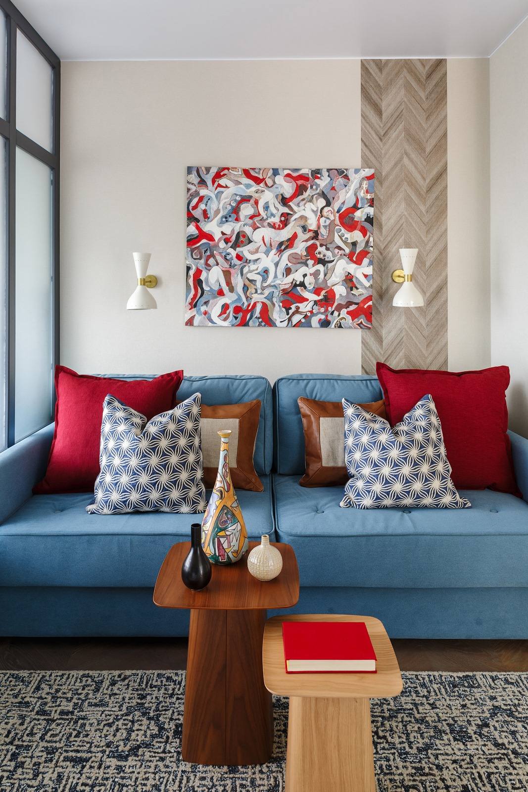 Phòng khách bố trí ghế sofa màu xanh lam, tô điểm những chiếc gối màu đỏ, nâu, xanh, trắng, kết hợp bức tranh trừu tượng như tổng hòa tất cả các màu sắc trên. Bộ bàn nước gỗ 2 tông màu đậm nhạt đơn giản mà tinh tế với những lọ gốm sứ trang trí.