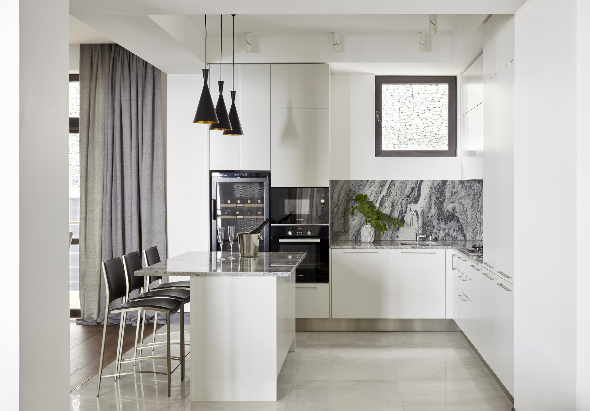 Dự án của nhà thiết kế Natalia Kühner với khu vực backsplash và toàn bộ mặt bàn bếp được ốp đá cẩm thạch vân xám sang trọng, tạo điểm nhấn cho không gian sử dụng gam màu trắng tươi sáng làm phông nền chủ đạo.