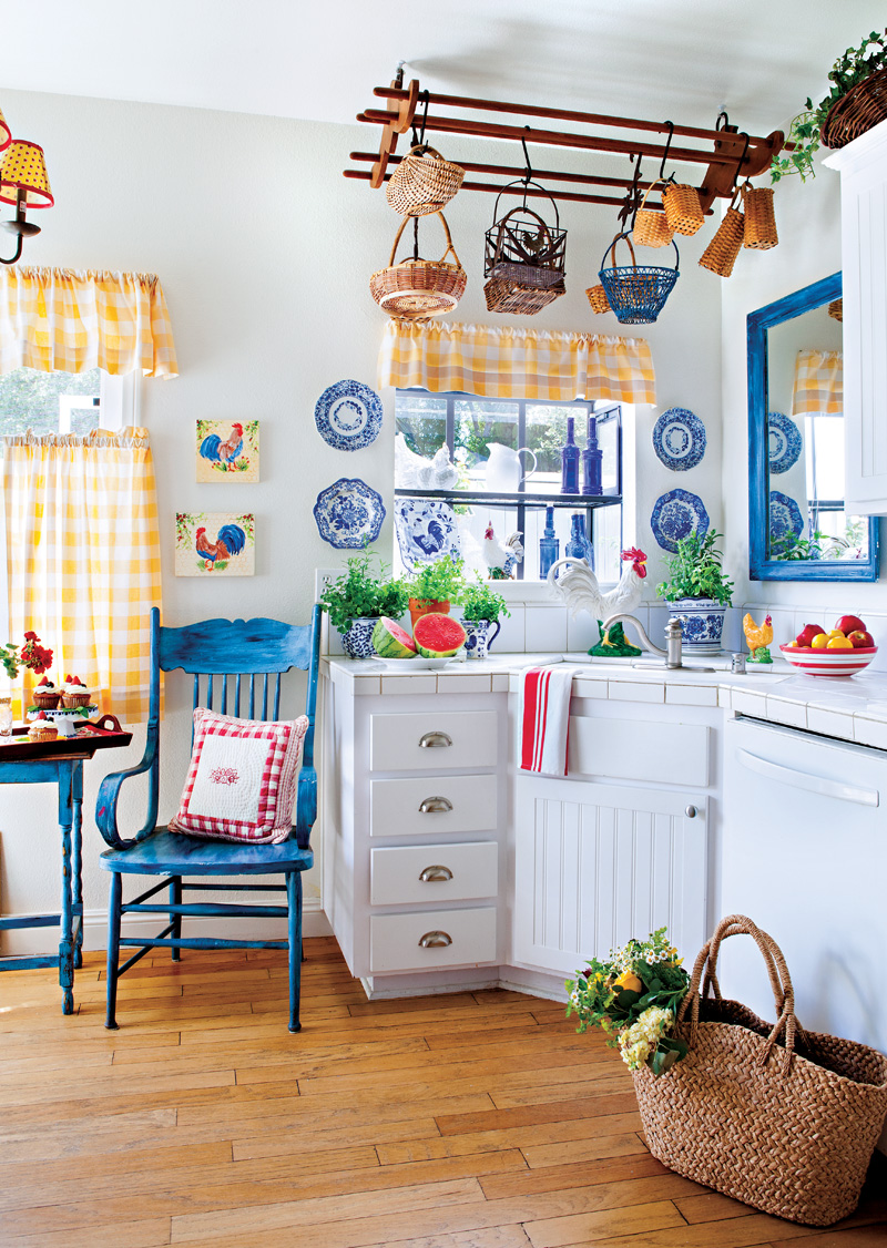 Phòng bếp nhỏ nhắn mà rực rỡ sắc màu. Ô cửa sổ treo rèm caro mang màu vàng của nắng. Tủ bếp, sơn tường trắng là phông nền hoàn hảo cho sắc xanh và đỏ trở nên nổi bật. Tấm gương, bàn ghế đều được sơn lại màu xanh lam để tạo nên sự đồng bộ.