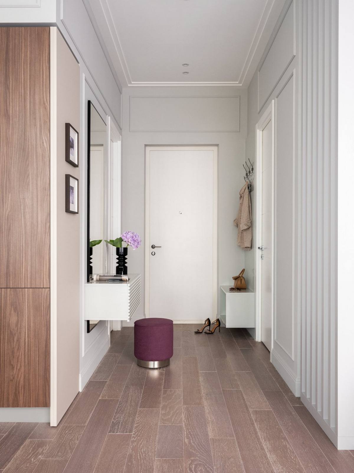 Lối vào căn hộ xinh đẹp với sàn gỗ tự nhiên nhẹ nhàng, chiếc ghế đôn màu tím nổi bật, một góc tường bố trí móc treo áo khoác và tủ đựng giày tiện lợi.
