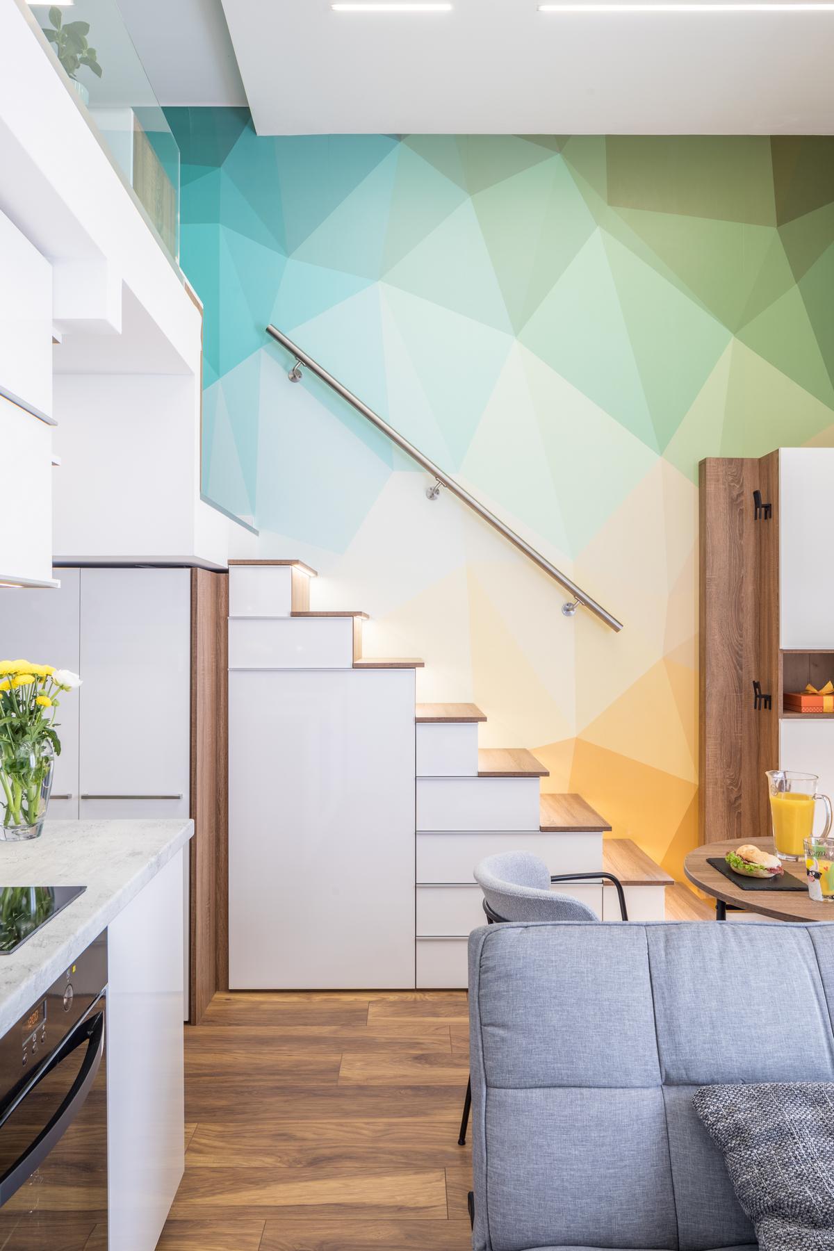 Tuy căn hộ có diện tích siêu nhỏ nhưng lại sở hữu trần nhà cao, đây là ưu điểm để nhà thiết kế nội thất tận dụng để thiết lập phòng ngủ trên gác lửng. Bức tường khu vực này được trang trí bằng họa tiết hình học nhiều màu pastel cam, xanh,... nổi bật.