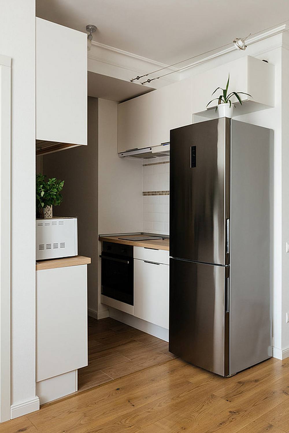 Phòng bếp được bố trí trong góc nhỏ của căn hộ, với hệ thống tủ lưu trữ màu trắng sạch sẽ, cùng với chiếc tủ lạnh cỡ lớn bằng thép không gỉ sáng bóng phản chiếu ánh sáng trên bề mặt thiết bị.