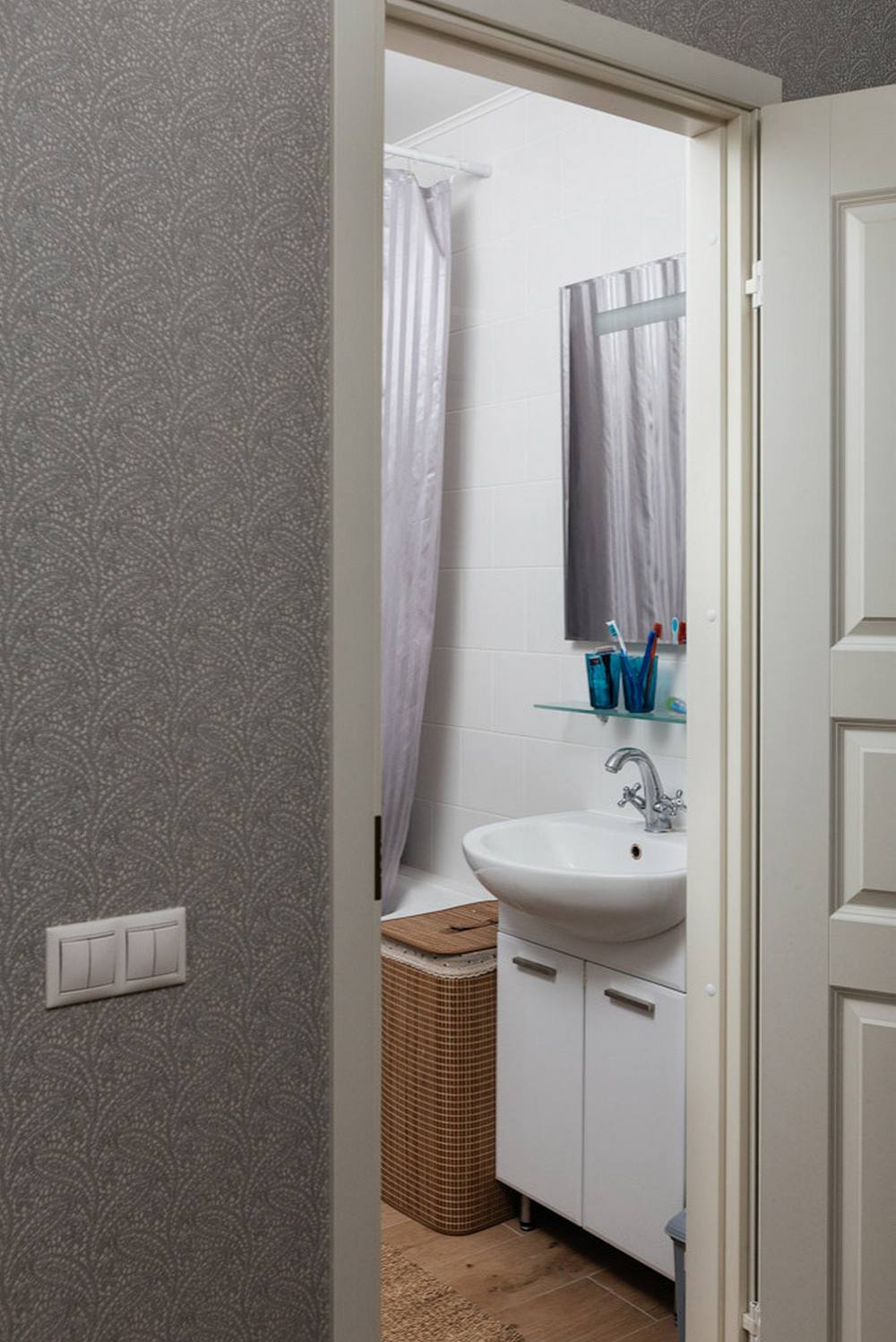Phòng tắm và nhà vệ sinh được bố trí đơn giản nhưng đầy đủ tiện nghi, hai khu vực này được phân vùng với nhau bởi tấm rèm che màu trắng kẻ sọc xám. Chiếc giỏ mây lưu trữ cũng là một yếu tố xinh xắn cho phòng tắm đáng yêu hơn.