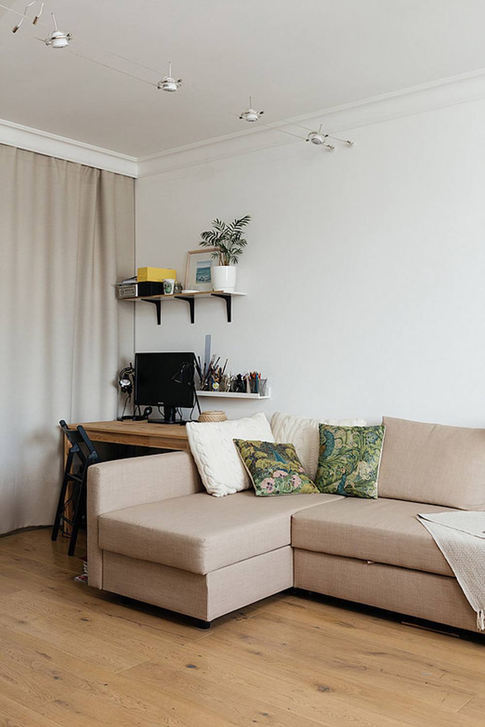 Toàn bộ bức tường trong căn hộ được sơn màu trắng tươi mới. Phòng khách thiết kế đơn giản với ghế sofa góc với gam màu be trang nhã. Kiểu sofa chữ L này cũng giúp 'phân chia ranh giới' giữa phòng khách và góc làm việc một cách hiệu quả.