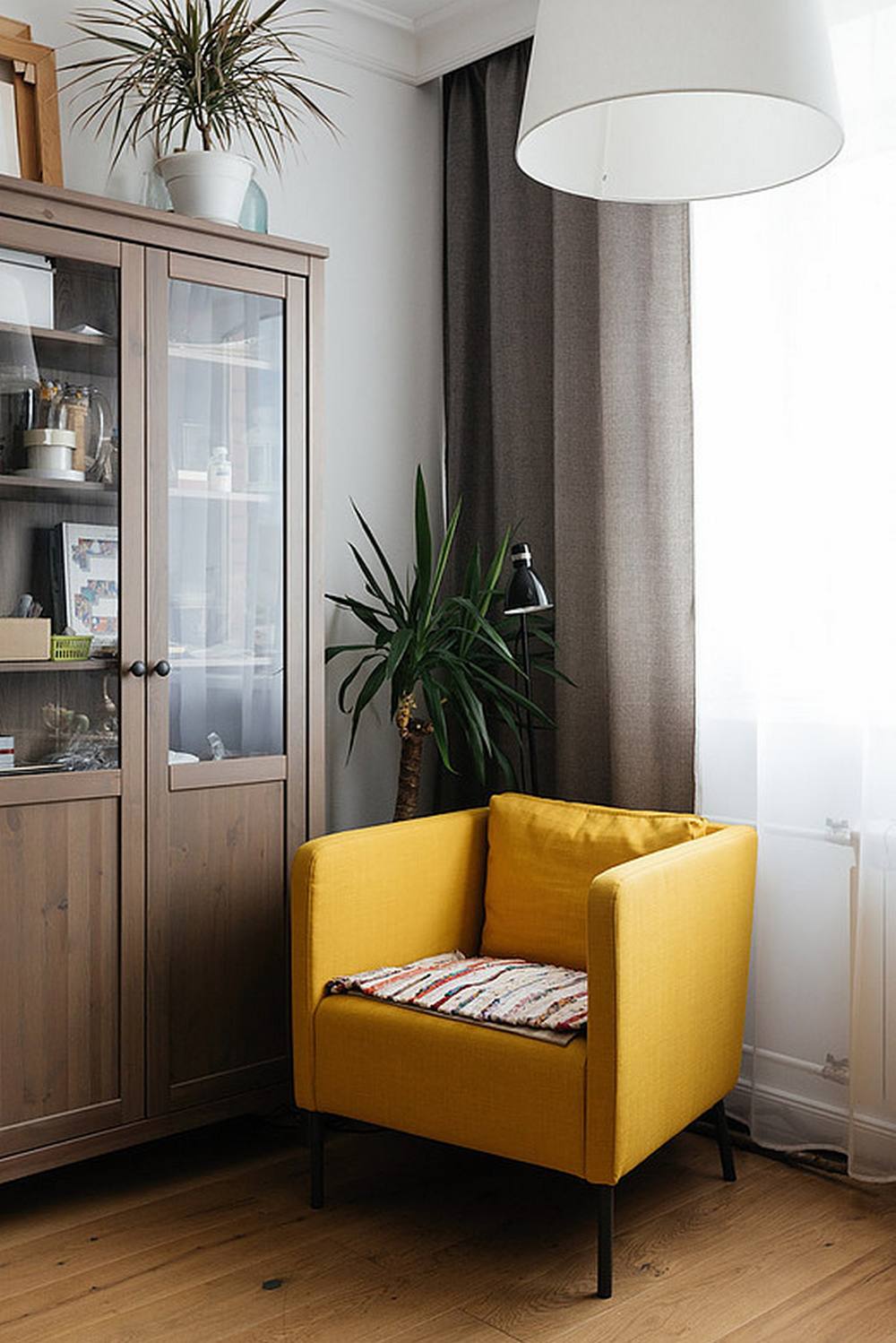 Một chiếc ghế bành màu vàng mù tạt nổi bật ở góc phòng khách, cạnh ô cửa sổ đầy nắng ấm, bố trí cùng với nó một chiếc đèn sàn dáng cao thanh mảnh tạo nên khu vực đọc sách tuyệt vời cho gia chủ.