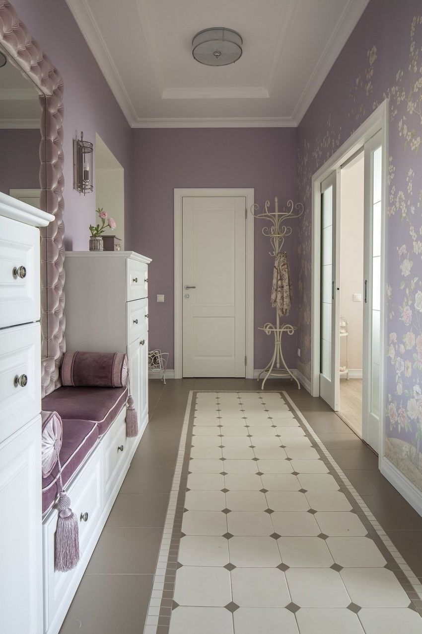 Hành lang căn hộ khá dài với gam màu tím mộng mơ, từ sơn tường cho đến giấy dán tường hoa văn nhẹ nhàng. Sàn nhà được lát gạch với cách sắp xếp giống như một tấm thảm trắng nổi bật trên nền xám.