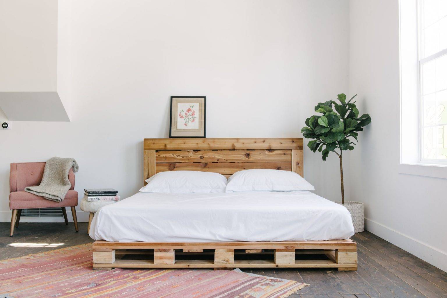 Phòng ngủ thiết kế theo phong cách minimalism (phong cách tối giản) với giường làm bằng gỗ pallet đặt ở vị trí trung tâm. Bên cạnh là chậu cây xanh tươi góp thêm sức sống cho căn phòng phủ đầy sắc trắng.
