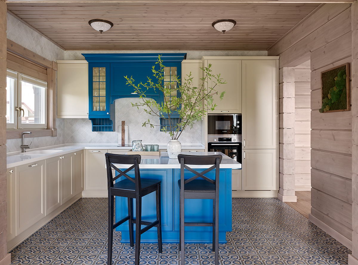 Sàn nhà thay đổi từ vật liệu gỗ đến lát gạch bông để phân vùng các khu vực chức năng bằng thị giác.  Đảo bếp và hệ tủ lưu trữ trong phòng bếp với màu xanh lam đậm nổi bật trên nền gạch bông màu xanh nhạt. 