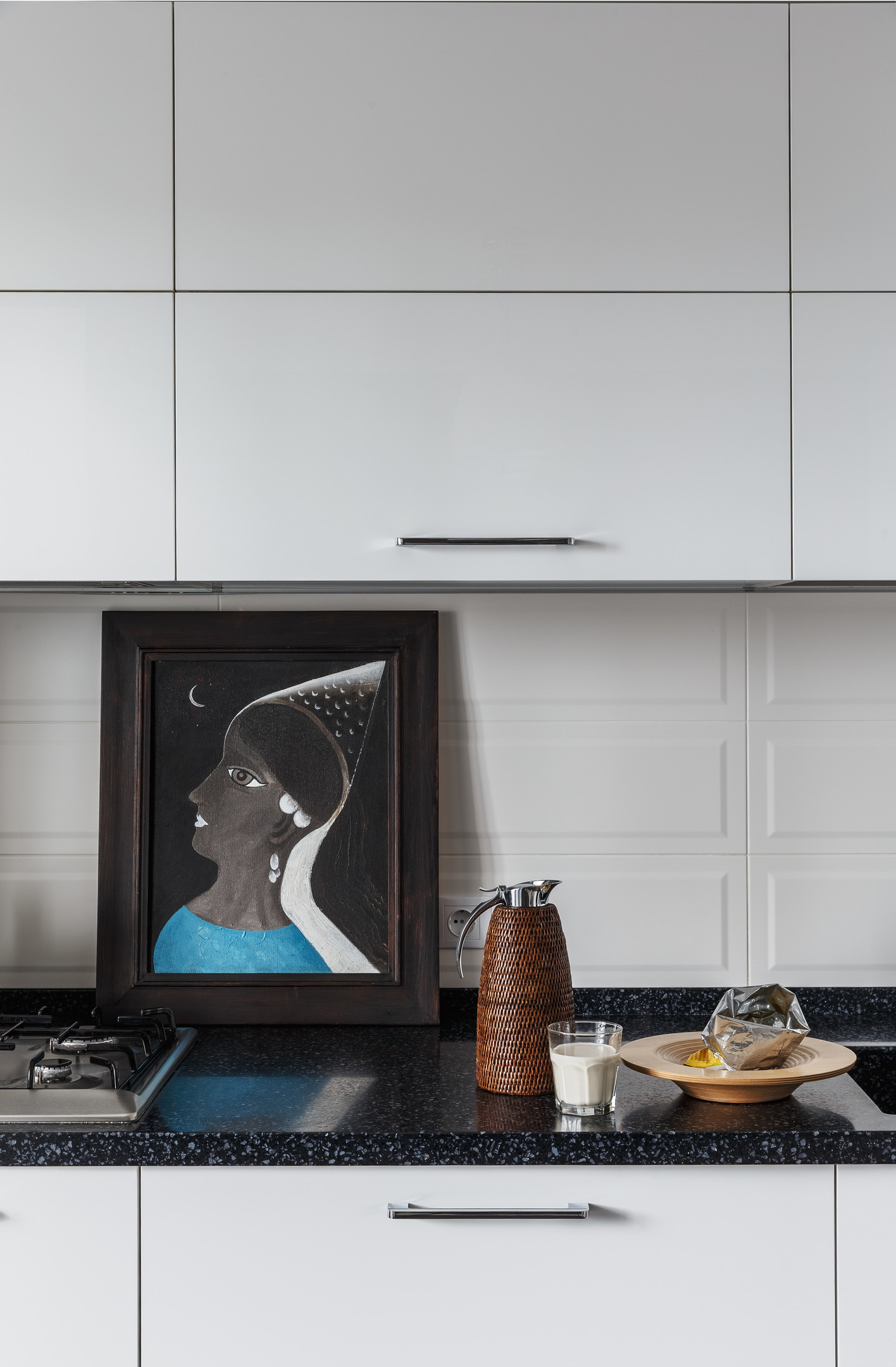 Phòng bếp sử dụng gạch lát sàn màu xám tương đồng với khu vực hành lang, tạo sự tương phản nhẹ nhàng với gam màu trắng chủ đạo của tường và tủ bếp.