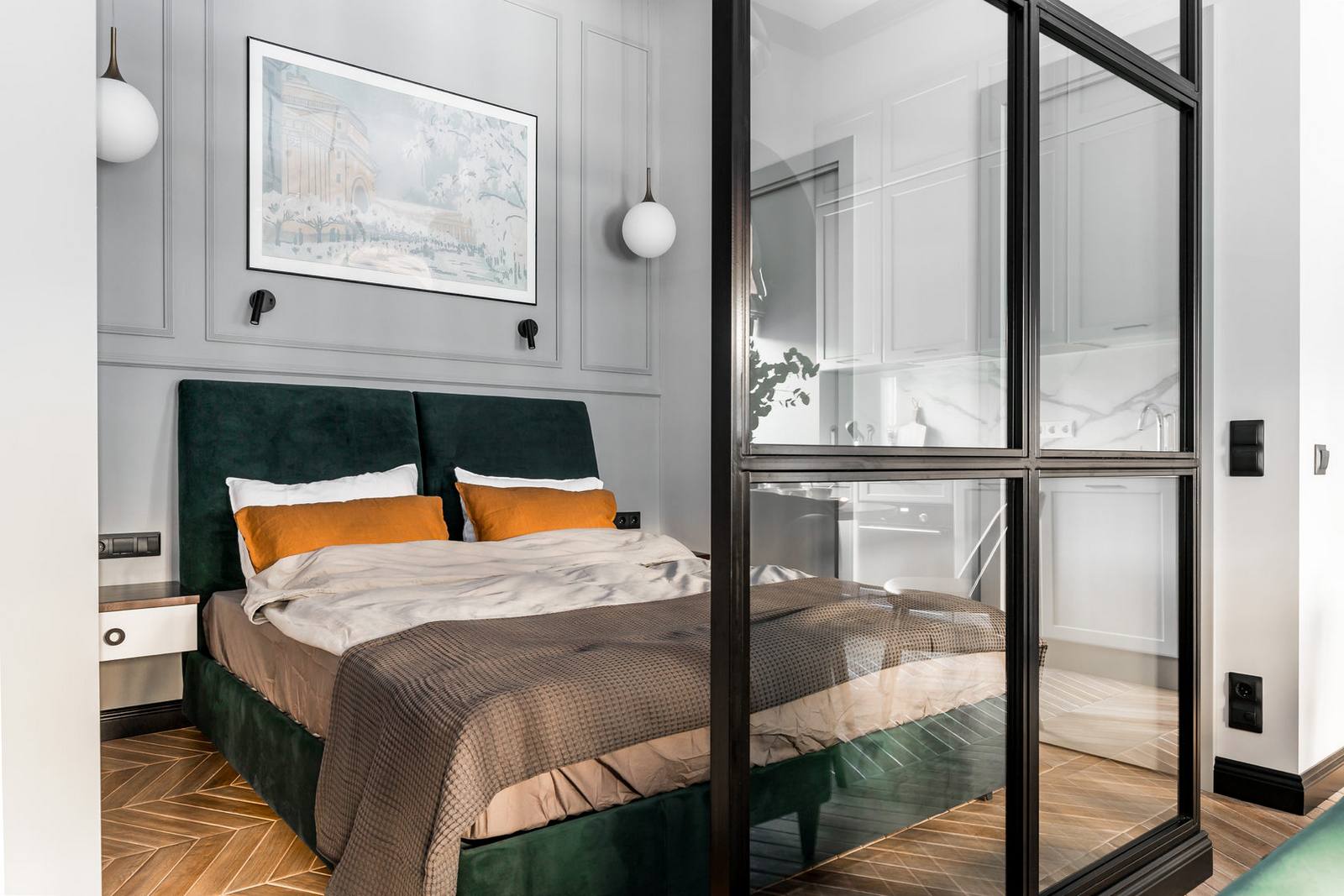 Khu vực phòng ngủ sử dụng khung giường bọc vải màu xanh ngọc lục bảo cùng những chiếc gối màu cam tạo sự kết nối bằng thị giác với phòng khách. Bức tranh thành phố của nước Nga xinh đẹp được trang trí ngay bức tường phía trên đầu giường.