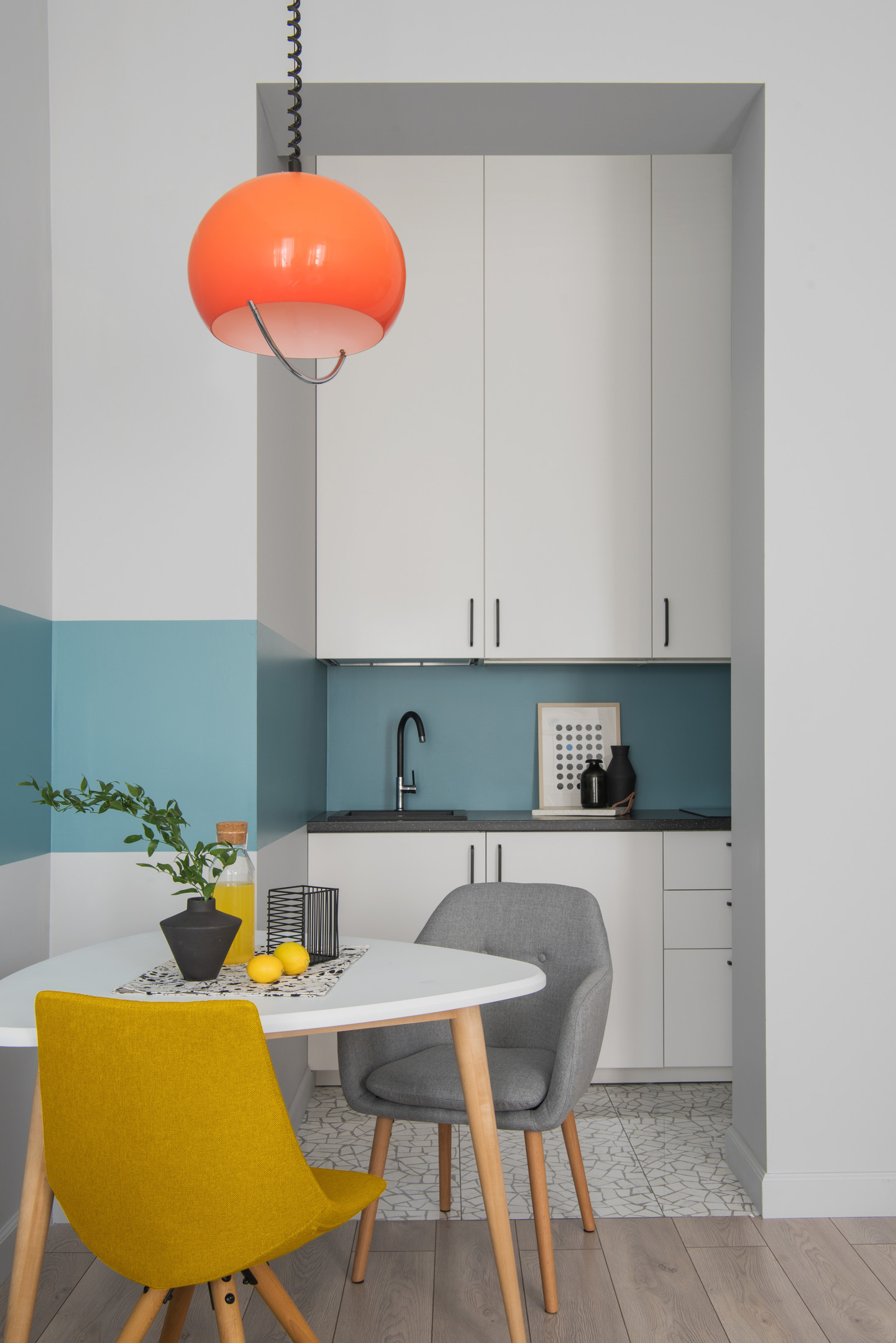 Dự án cải tạo căn hộ của NTK Sveta Khabeeva đặc biệt nhấn mạnh đến khả năng sử dụng sắc màu làm điểm nhấn. Dải sơn màu xanh lam “chạy ngang” nền tường trắng, cặp ghế xám - vàng mù tạt kết hợp với đèn thả trần màu cam. Chiếc đèn tròn trịa, xinh xắn không chỉ chiếu sáng mà còn trang trí cho căn phòng thêm bắt mắt.
