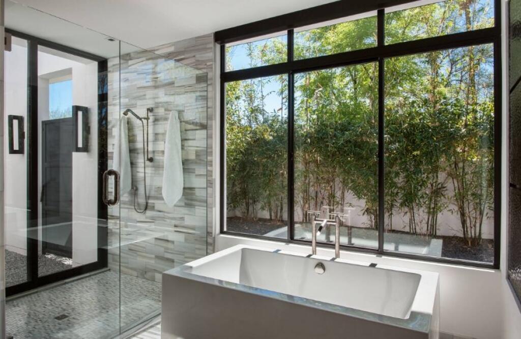 Và cuối cùng là phòng tắm rộng rãi, sang chảnh với buồng tắm đứng và bồn tắm nằm phân vùng bằng cửa kính trong suốt. Bức tường kính viền khung đen nhìn ra khu vườn của gia đình nên vẫn đảm bảo sự riêng tư nhất định trong phạm vi ngôi nhà.