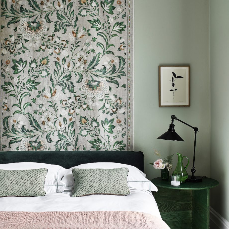 Phòng ngủ cuốn hút với một tấm vải hoa văn nền nã, trang trí khu vực đầu giường thay cho tranh ảnh hay giấy dán tường quen thuộc. cả chiếc táp đầu giường và bình cắm hoa cũng mang màu xanh ngọc lục bảo đẹp mắt.