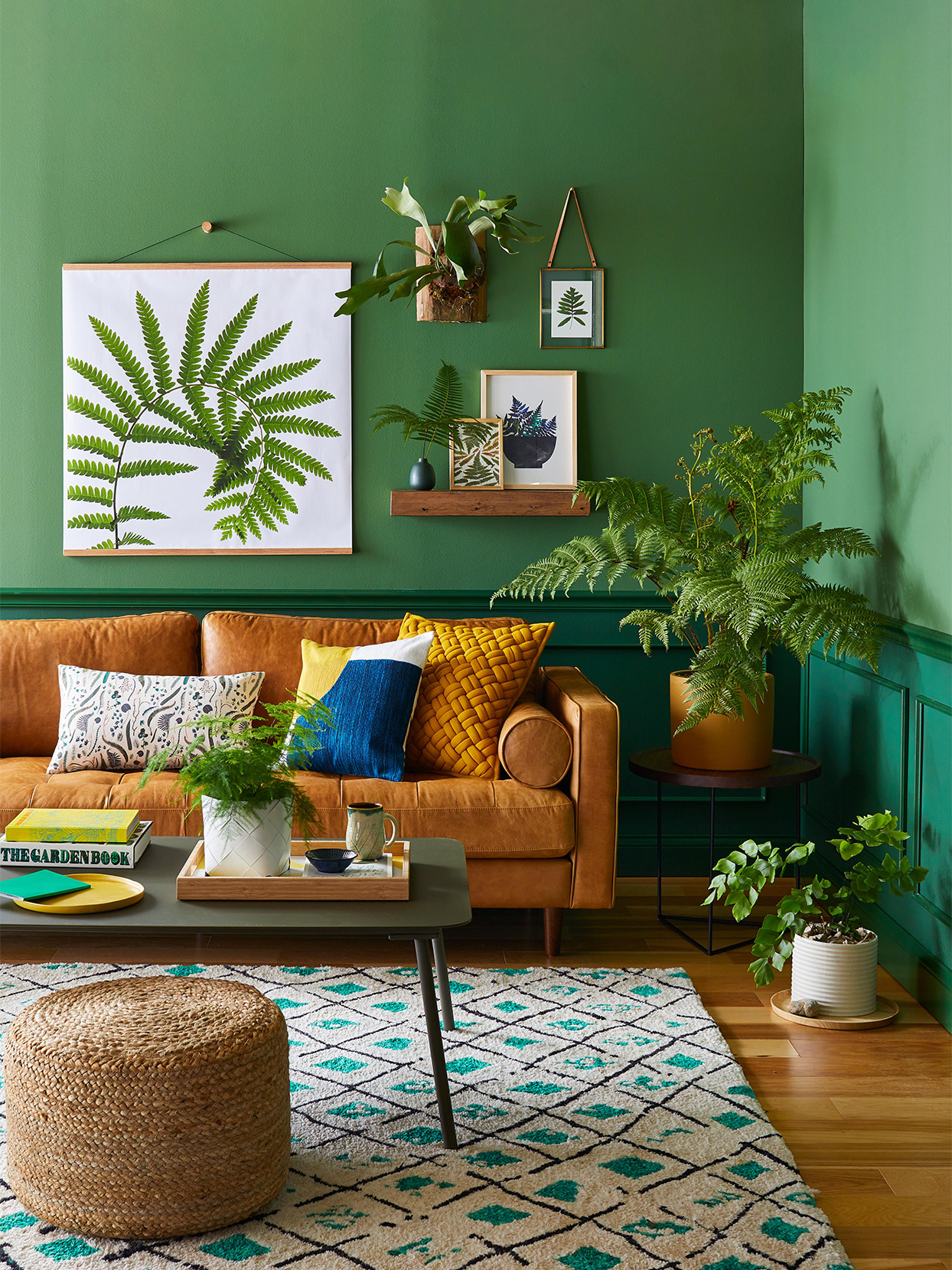 Phòng khách mùa Hè sử dụng 2 sắc thái xanh lá cây - xanh ngọc lục bảo trang trí bức tường, làm phông nền để sofa màu nâu ấm áp trở nên nổi bật. Những tán lá dương xỉ từ trên tranh đến thực tế giúp cho phòng khách nhỏ xinh nhưng sống động vô cùng!