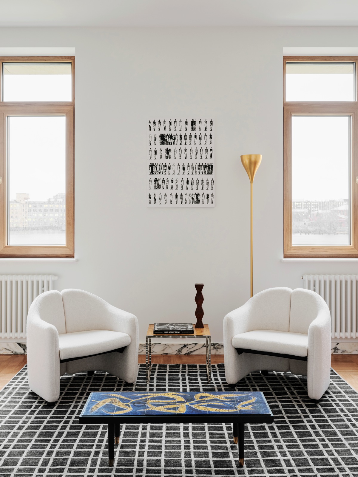 Toàn bộ bức tường trong căn hộ được sơn trắng cho vẻ đẹp tươi sáng, kết hợp dễ dàng với nội thất xung quanh. Thay vì sử dụng sofa cỡ lớn, NTK đã chọn 2 chiếc ghế bành nhỏ, 1 bàn nước hình chữ nhật với mặt bàn màu xanh lam và họa tiết lạ mắt. Chính giữa là bàn phụ nhỏ nhắn, trên tường là bức tranh của họa sĩ Alina Utrobina.