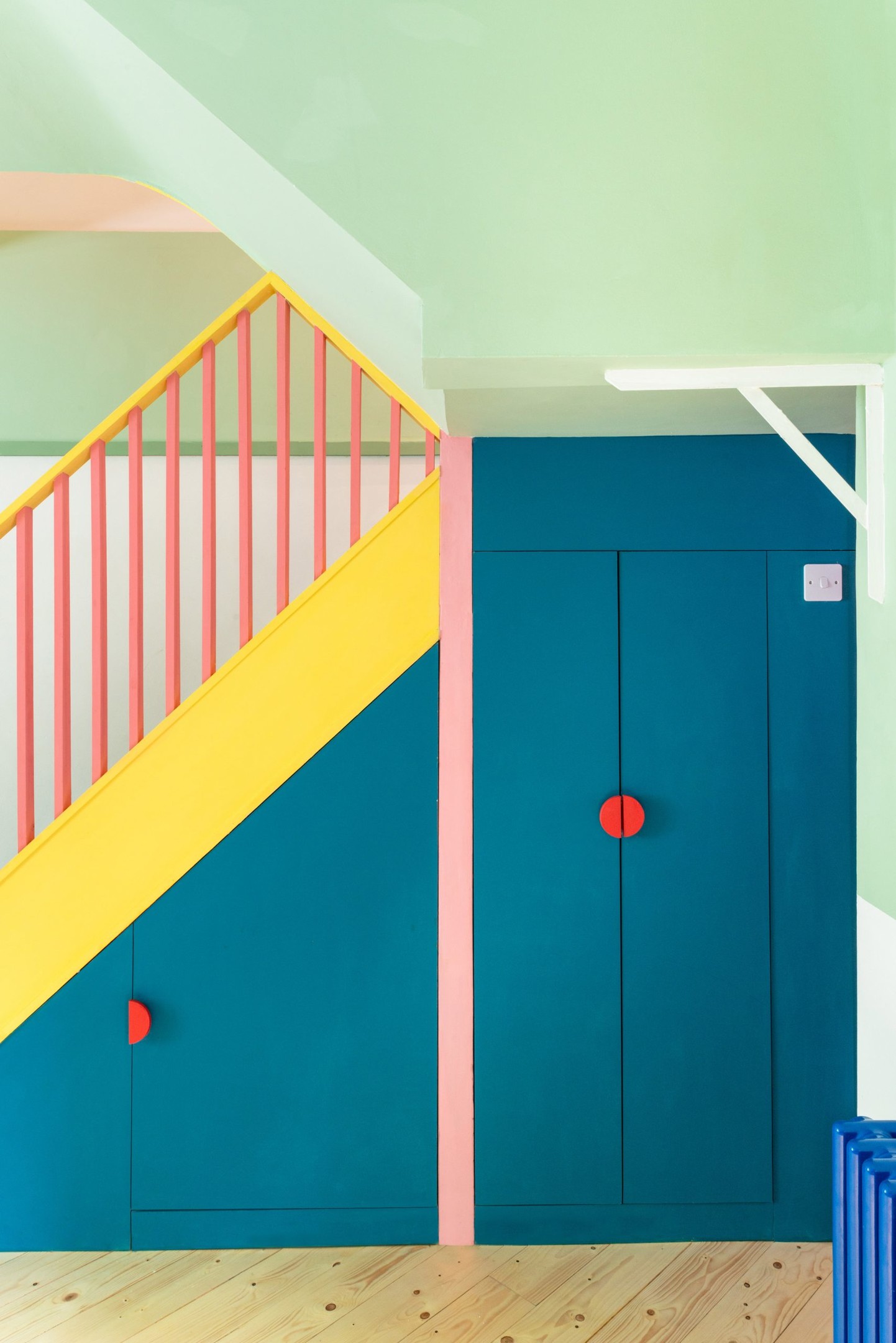 Khu vực cầu thang dẫn lối lên tầng 2 ngôi nhà lựa chọn màu xanh lam đậm chủ đạo, từ các bậc tam cấp cho đến mặt bên. Đặc biệt, các nhà thiết kế đã tích hợp hệ thống tủ lưu trữ nhằm tối ưu hóa không gian với tay nắm cửa màu đỏ làm điểm nhấn.