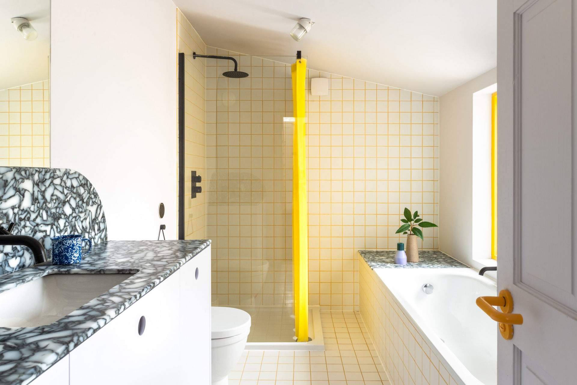 Phòng tắm kết hợp nhà vệ sinh trên tầng 2 của ngôi nhà sử dụng gam màu trắng và vàng tươi sáng như màu của nắng, kết hợp với ánh sáng từ ô cửa sổ càng thêm phần tươi mới. Bề mặt bồn rửa ốp đá granite tự nhiên tạo điểm nhấn về màu sắc cho không gian.