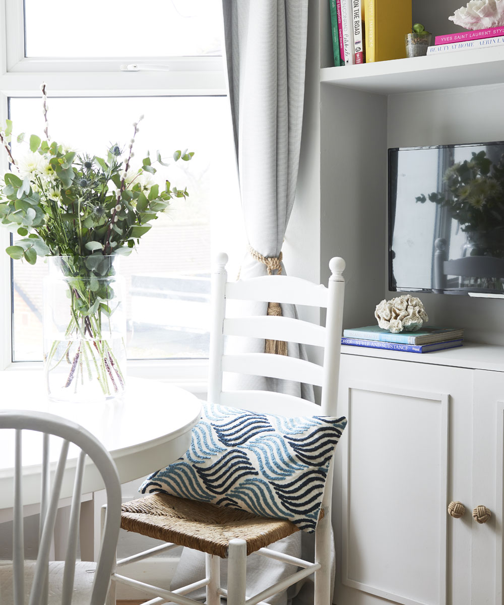 Một bộ bàn ghế dành cho khu vực ăn sáng và đọc sách được bố trí ngay cạnh ô cửa sổ đầy nắng ấm với rèm che mềm mại cùng lọ cắm hoa bằng thủy tinh đẹp mắt. 