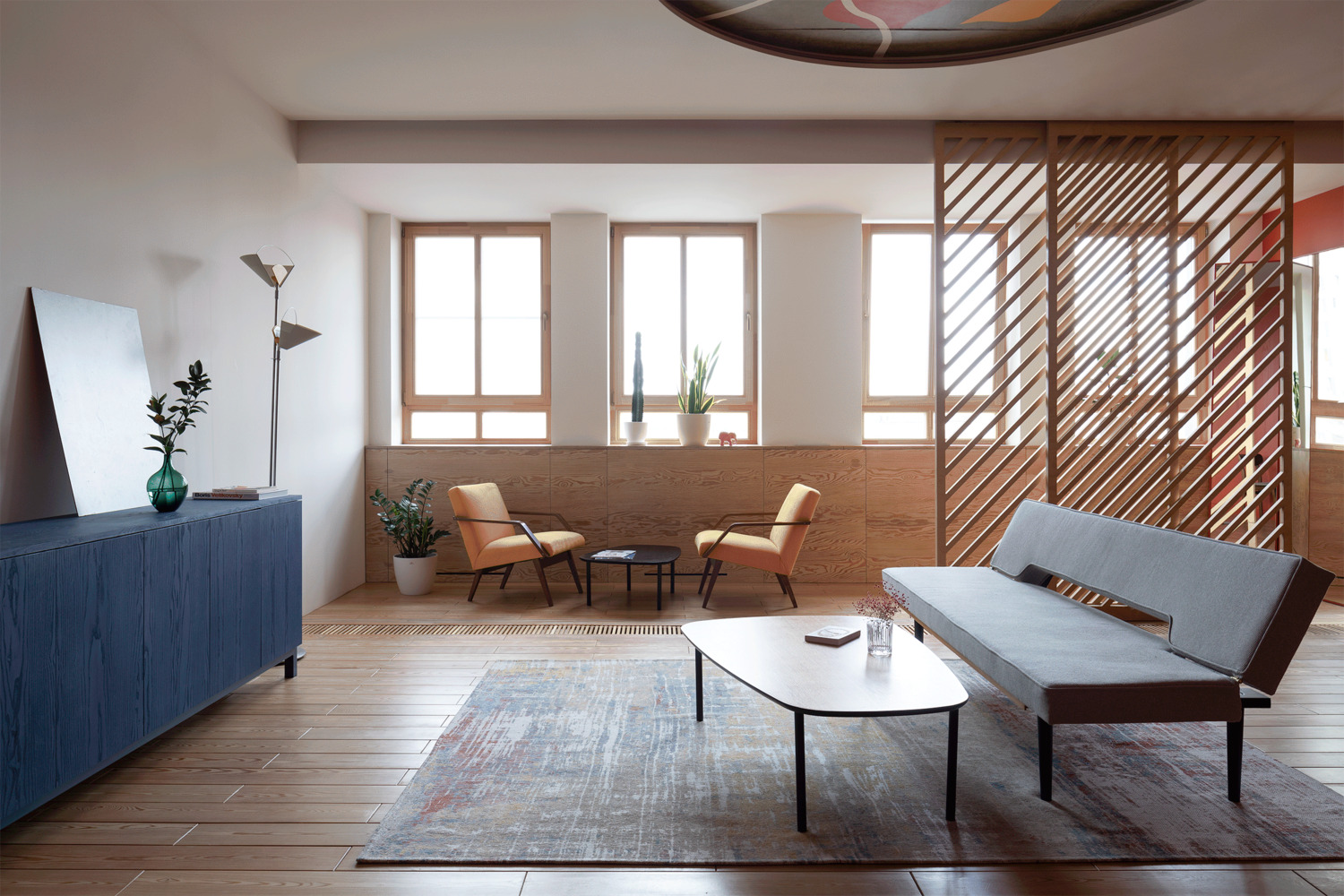 Phòng khách chính với chiếc ghế dài màu xám cùng bàn nước thiết kế đơn giản, tất cả được bố trí gọn gàng trên một tấm thảm trải sàn trên nền nhà gỗ.